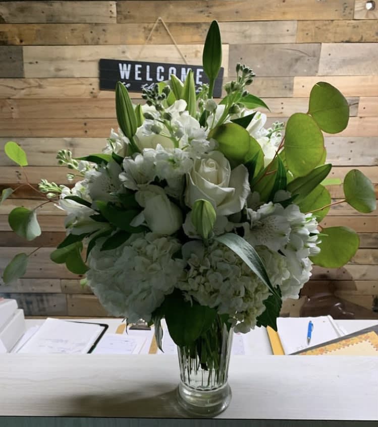 White floral arrangement in a clear glass vase with green foliage