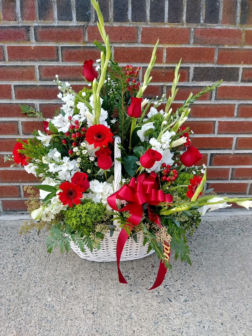 Basket arrangement of red roses, white flowers, and a red ribbon