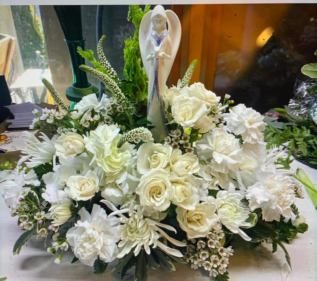White floral arrangement with roses and carnations around a figurine centerpiece