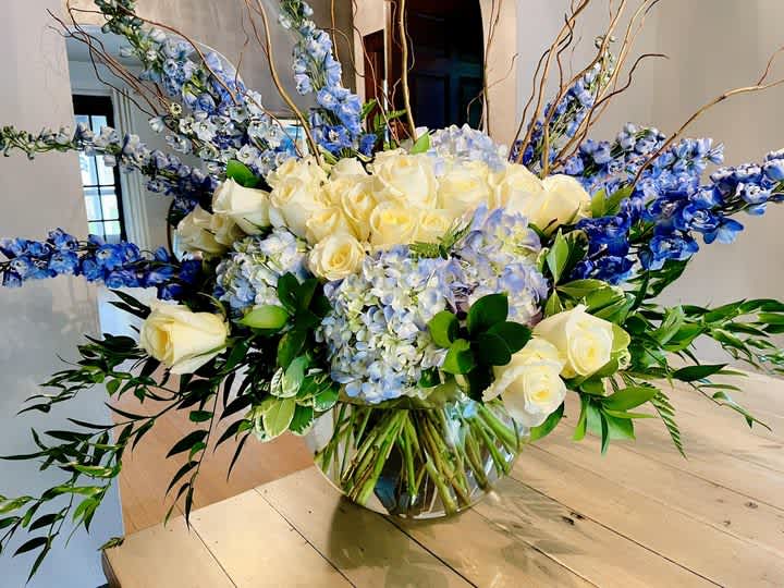 Large bouquet of cream roses, blue flowers, and hydrangeas in a glass vase