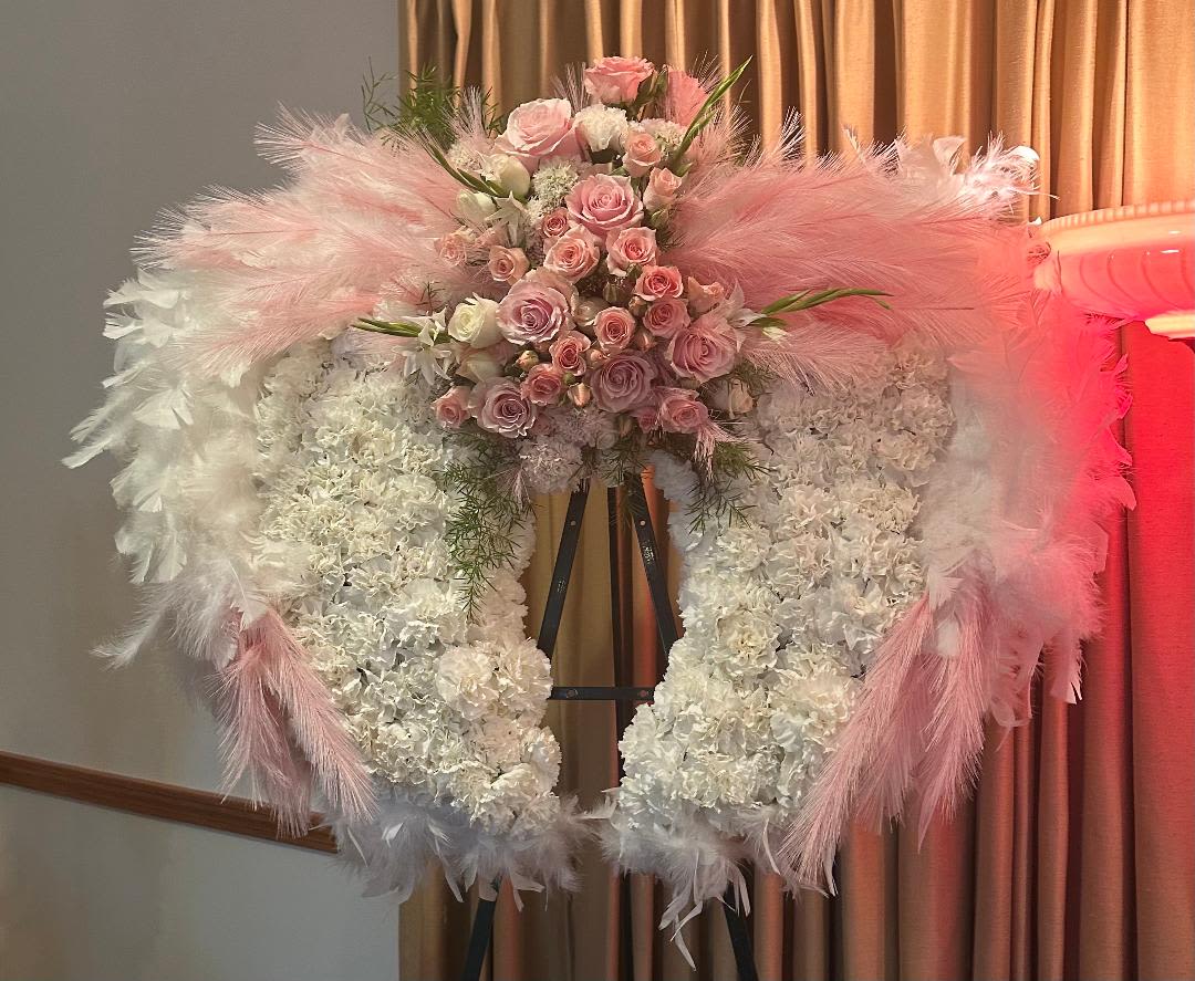 Pink and white floral wreath on an easel with feather accents