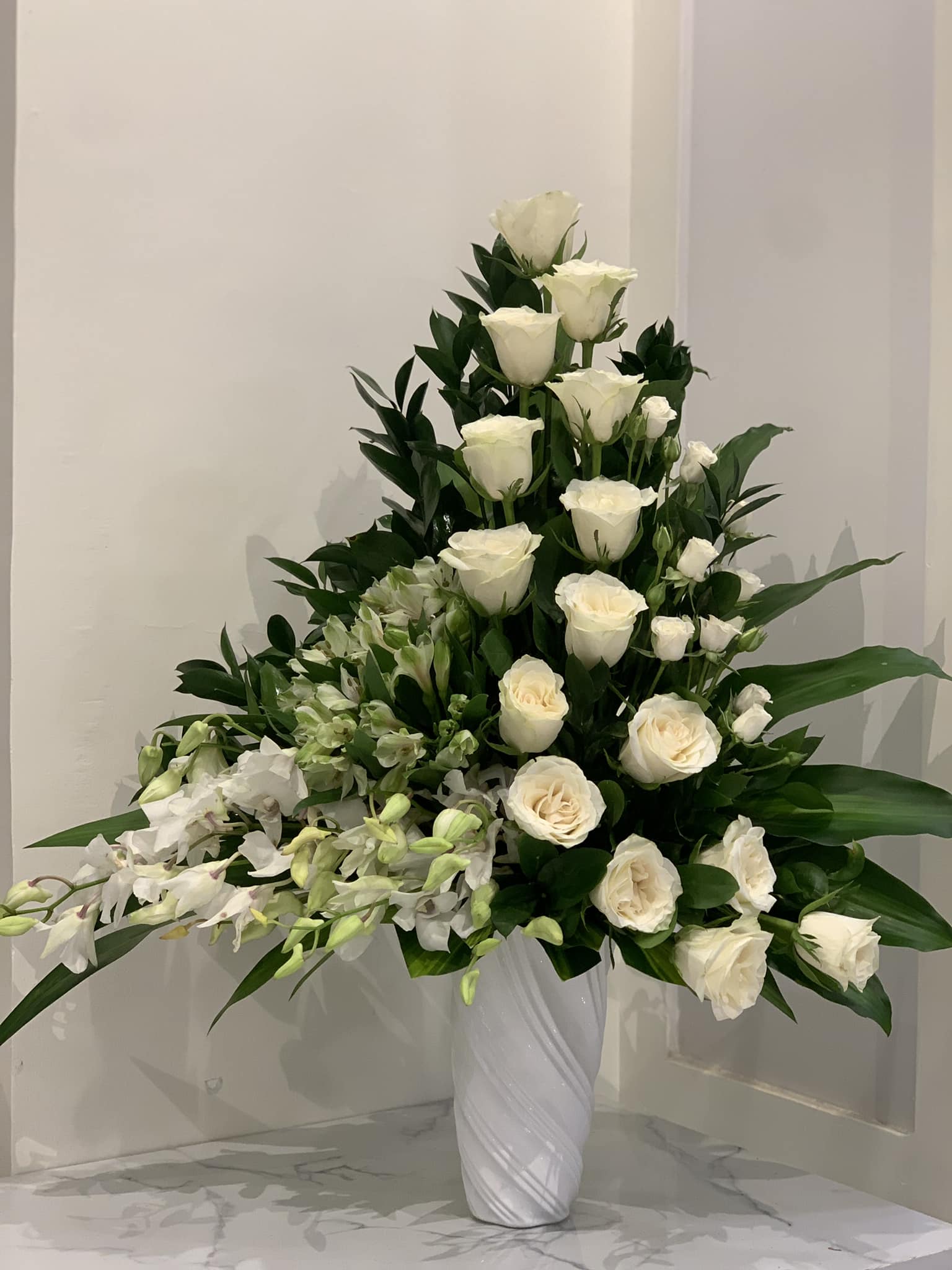 Tall white rose arrangement with orchids in a white vase