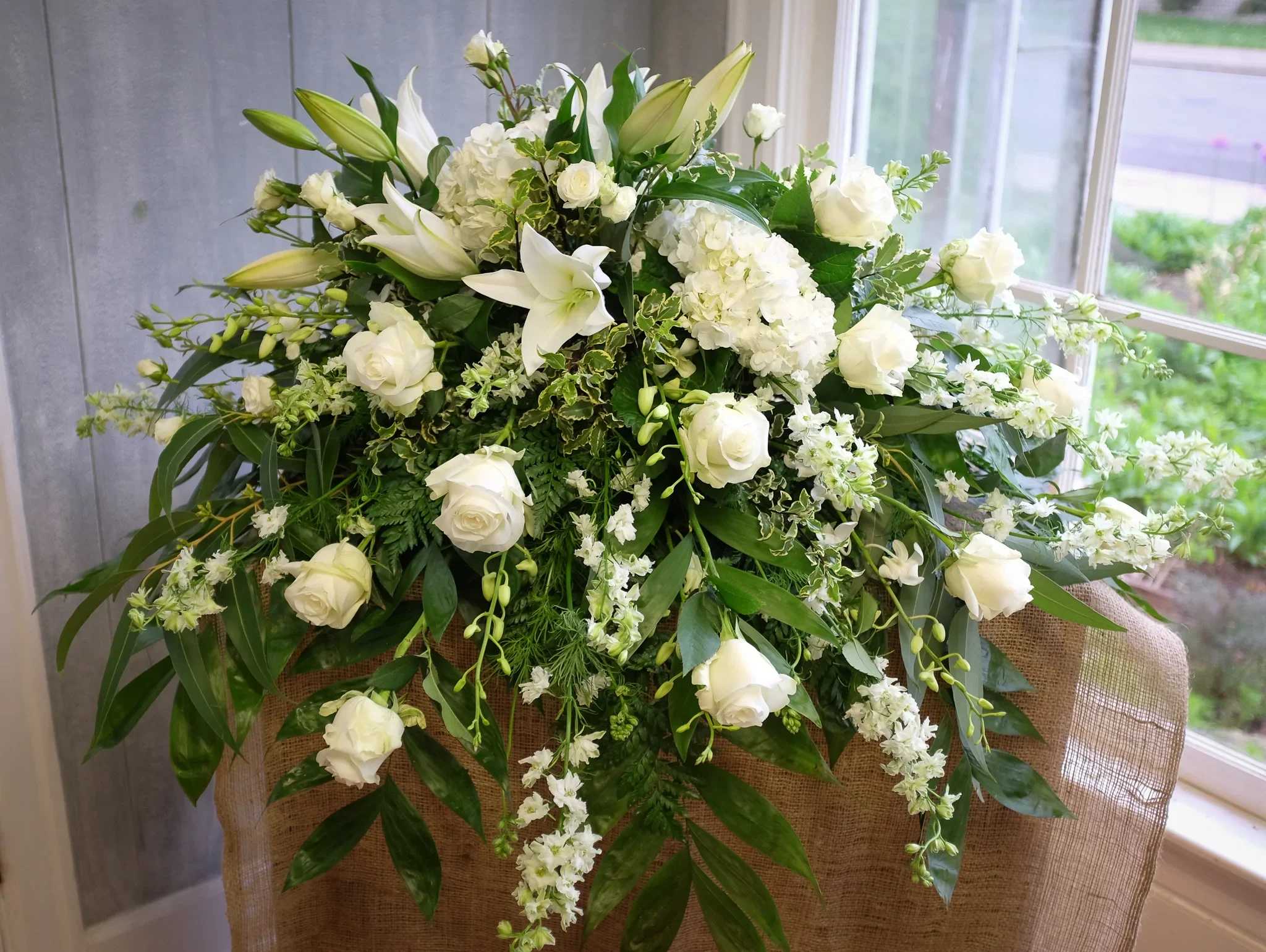 White floral arrangement with roses and lilies on a burlap-covered stand