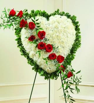 Heart-shaped white floral wreath with red roses on a stand