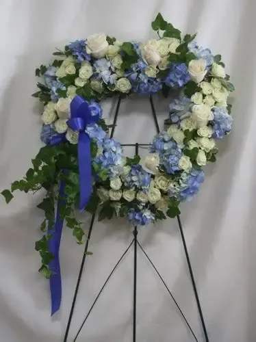Blue and white floral wreath on a black easel with a purple ribbon