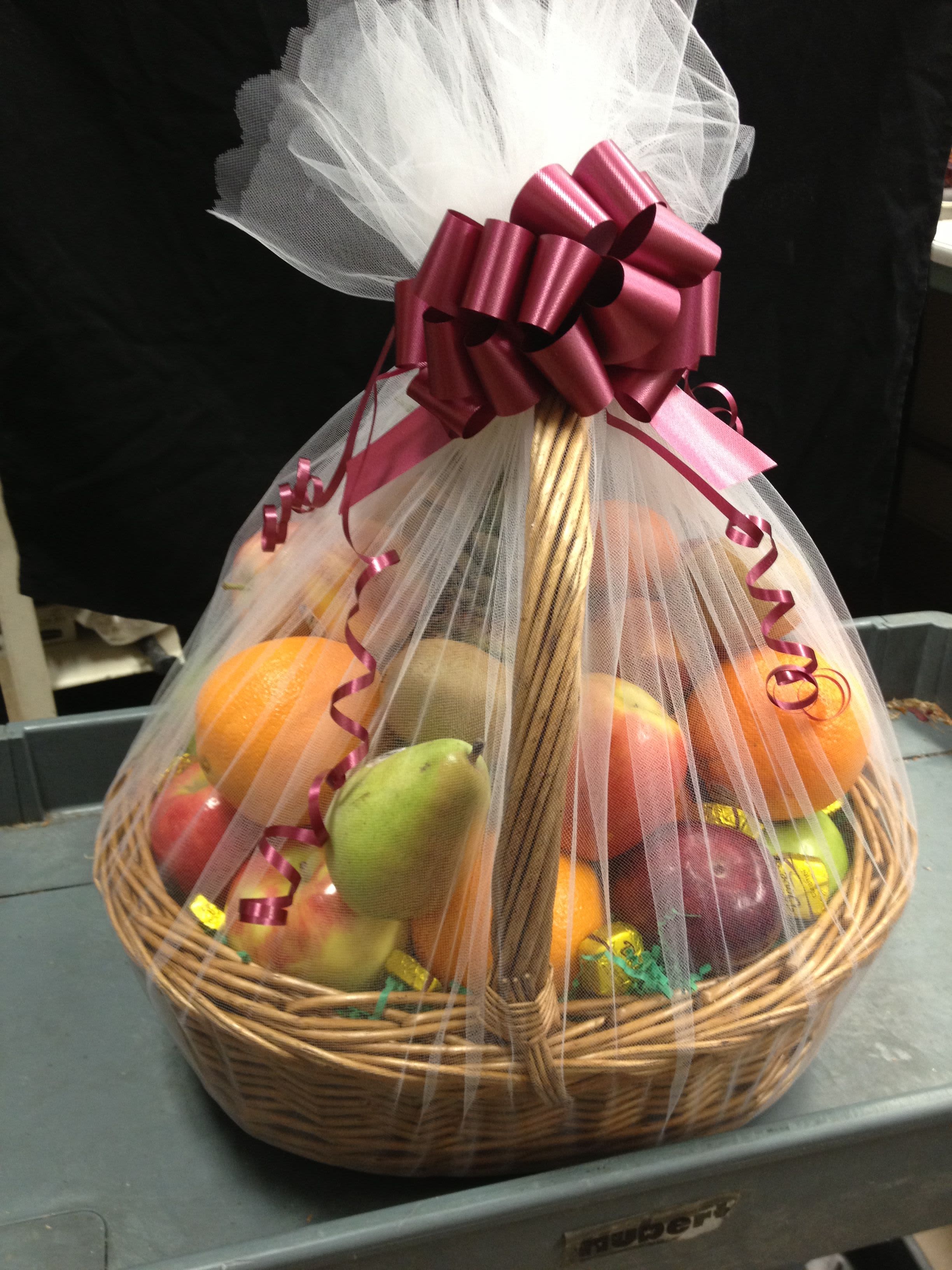 Fruit basket wrapped in white tulle with a burgundy bow