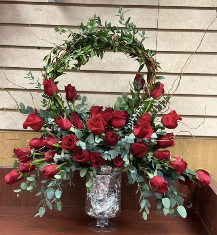 Red roses arranged in a tall vase with a leafy arch above