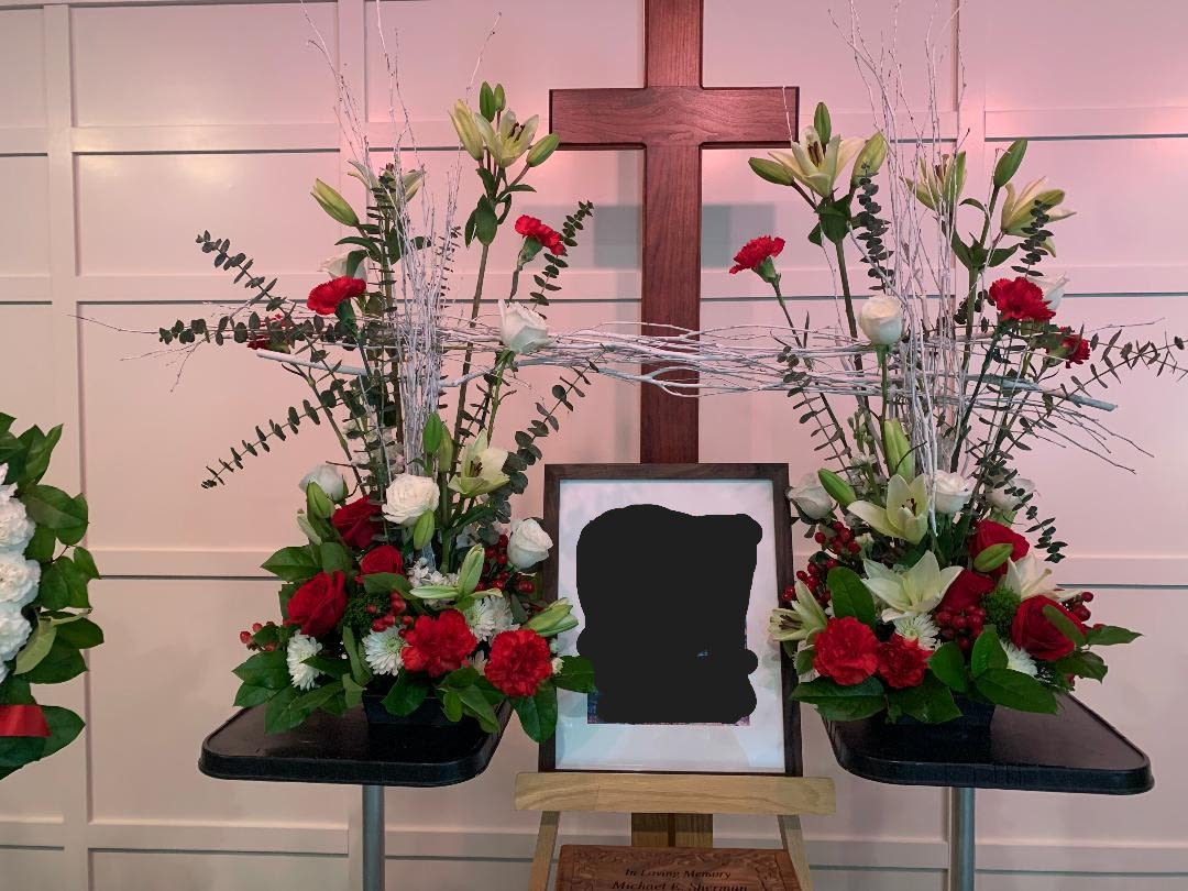 Symmetrical funeral floral display with red and white flowers around a framed photo and cross