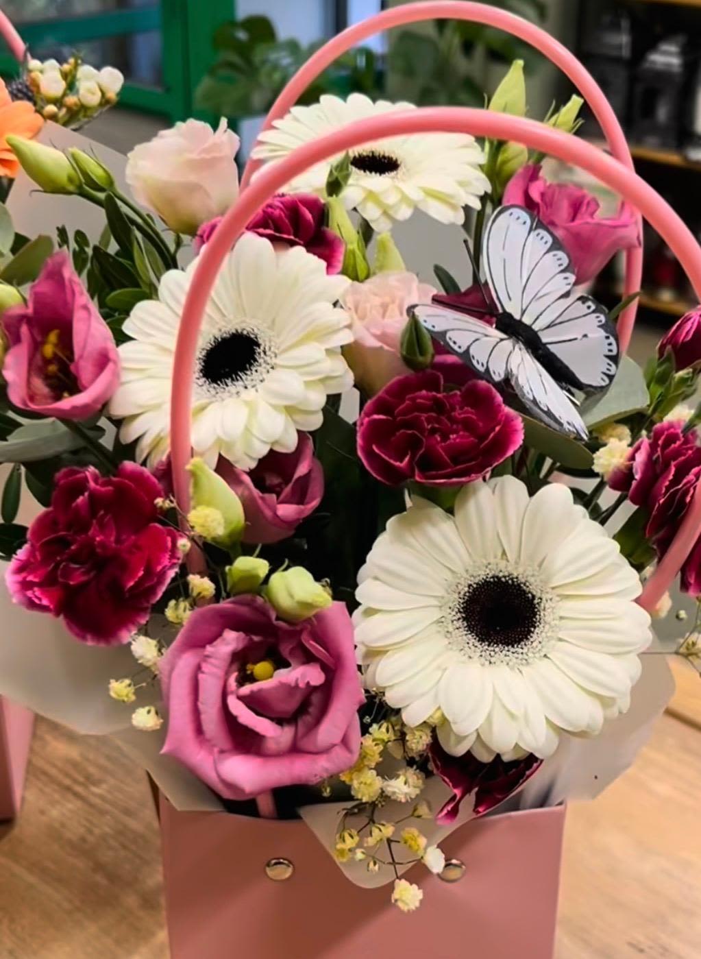 Pink and white mixed flower arrangement with gerbera daisies and carnations in a pink handled box with a butterfly decoration.