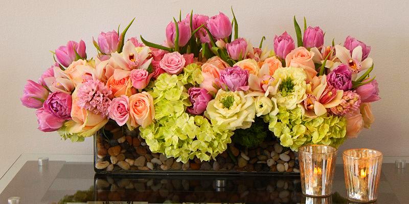 Spring Pastel Vase - Long glass vase, filled with Pastel colored Orchids, Roses, Hydrangeas, Tulips and Hyacinths and a bed of rocks. This spectacular design will instantly become the centerpiece of any room. Approx. 24" Long by 9" Tall