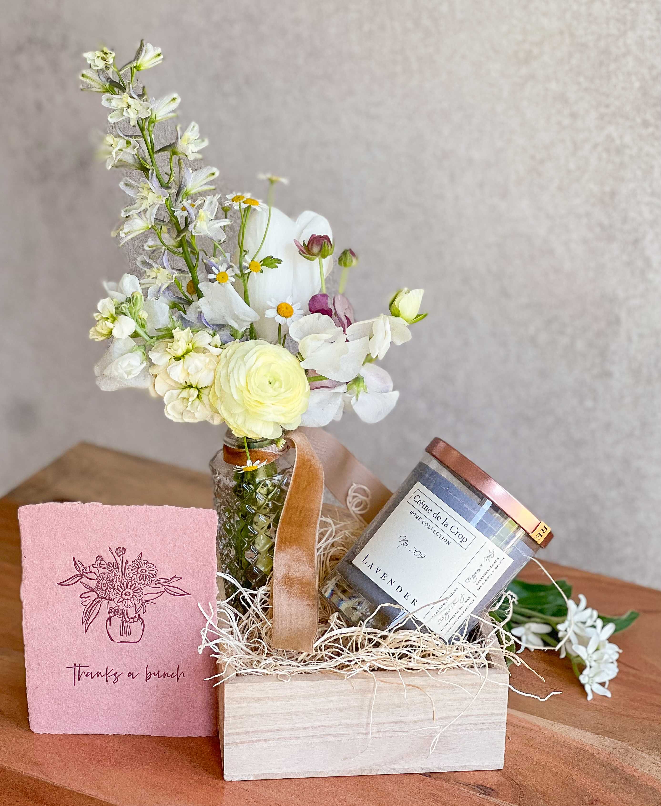 Small flower arrangement in a glass jar with a candle and pink card in a gift box