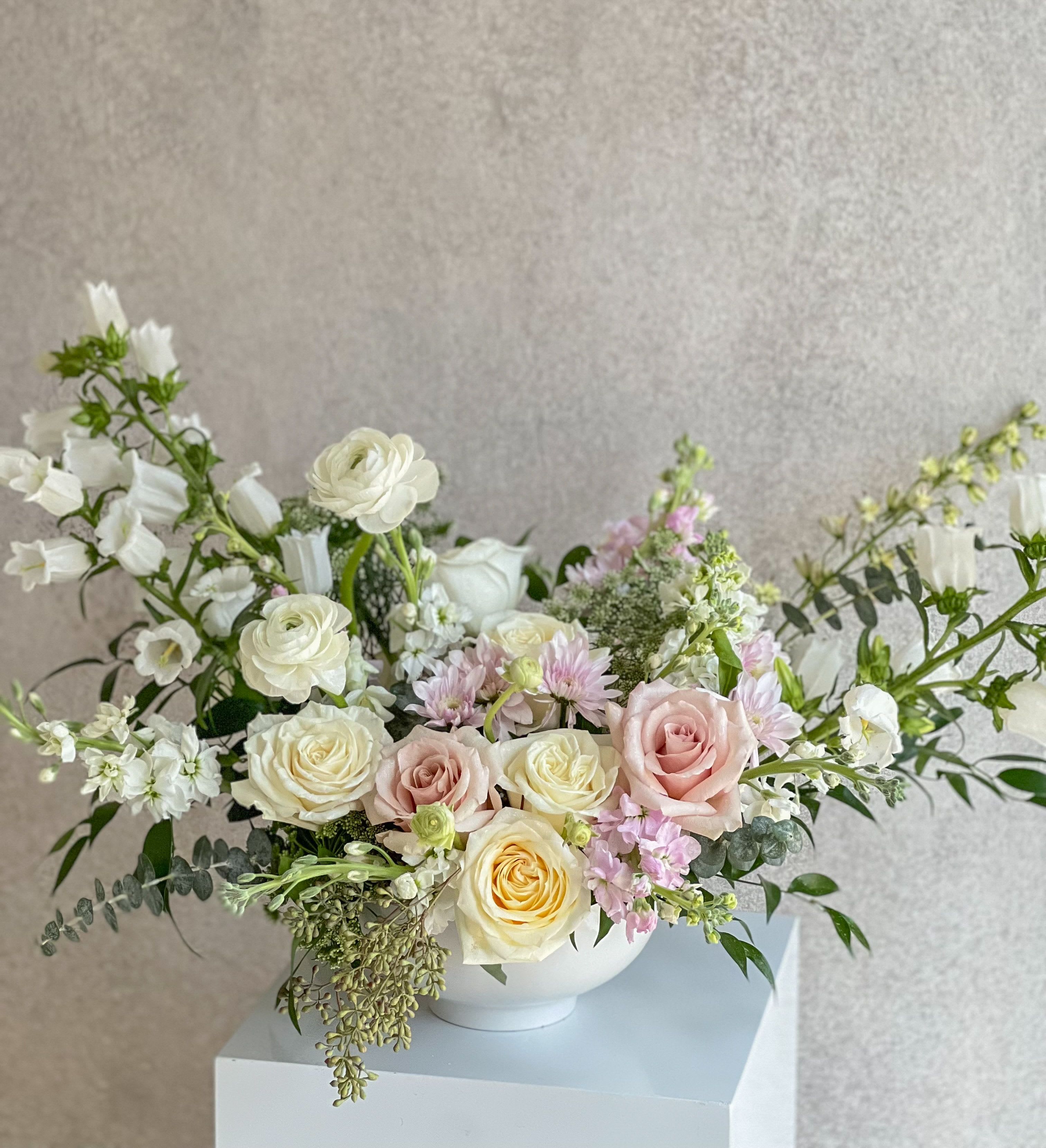 Pastel bouquet of roses and white blooms in a white bowl vase