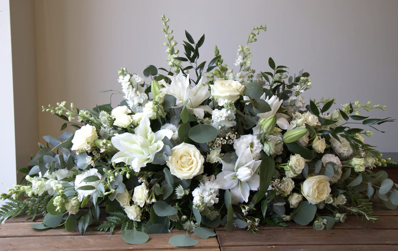 White Serenity Casket Spray  - An all white tribute, this full casket spray is pure and tranquil. Featuring a variety of white flowers and greenery.  Pictured is the Standard 