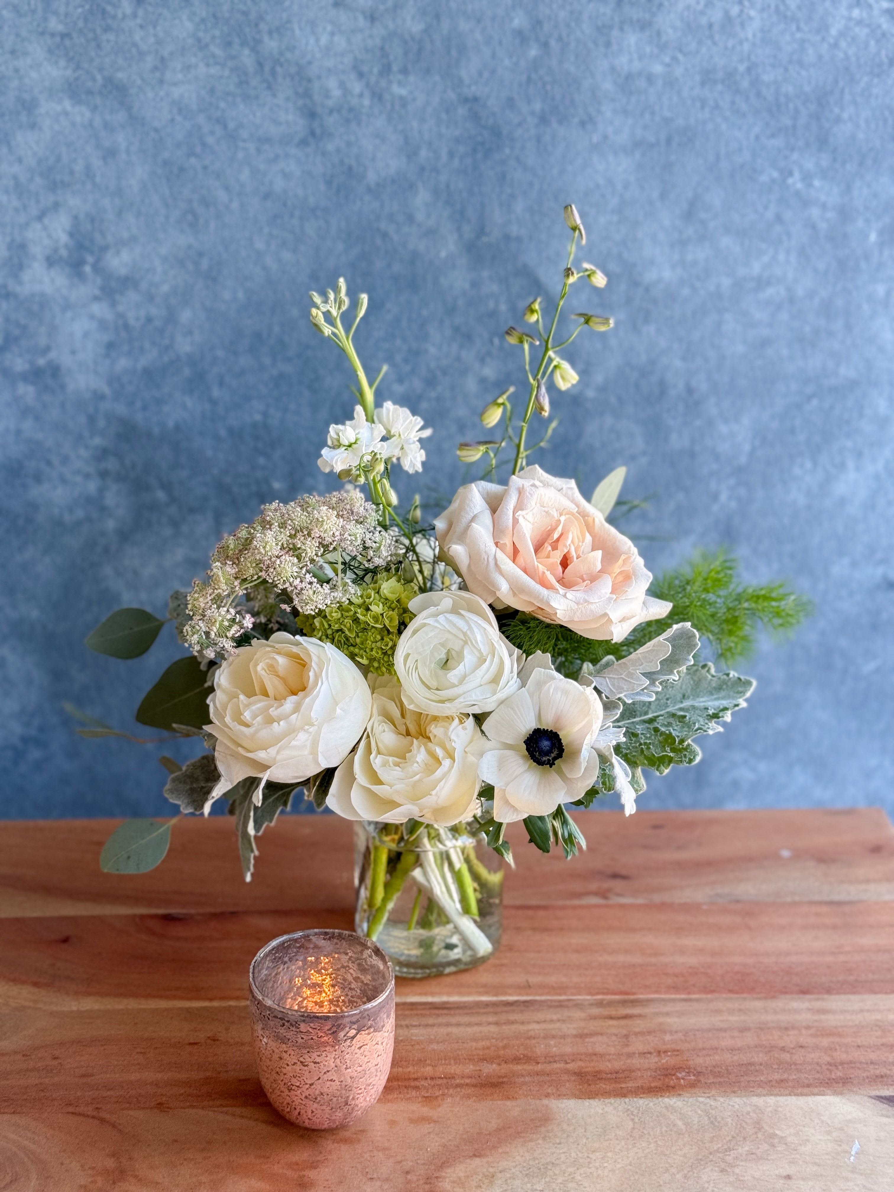 Cream and blush flowers arranged in a clear glass vase with a candle in front.