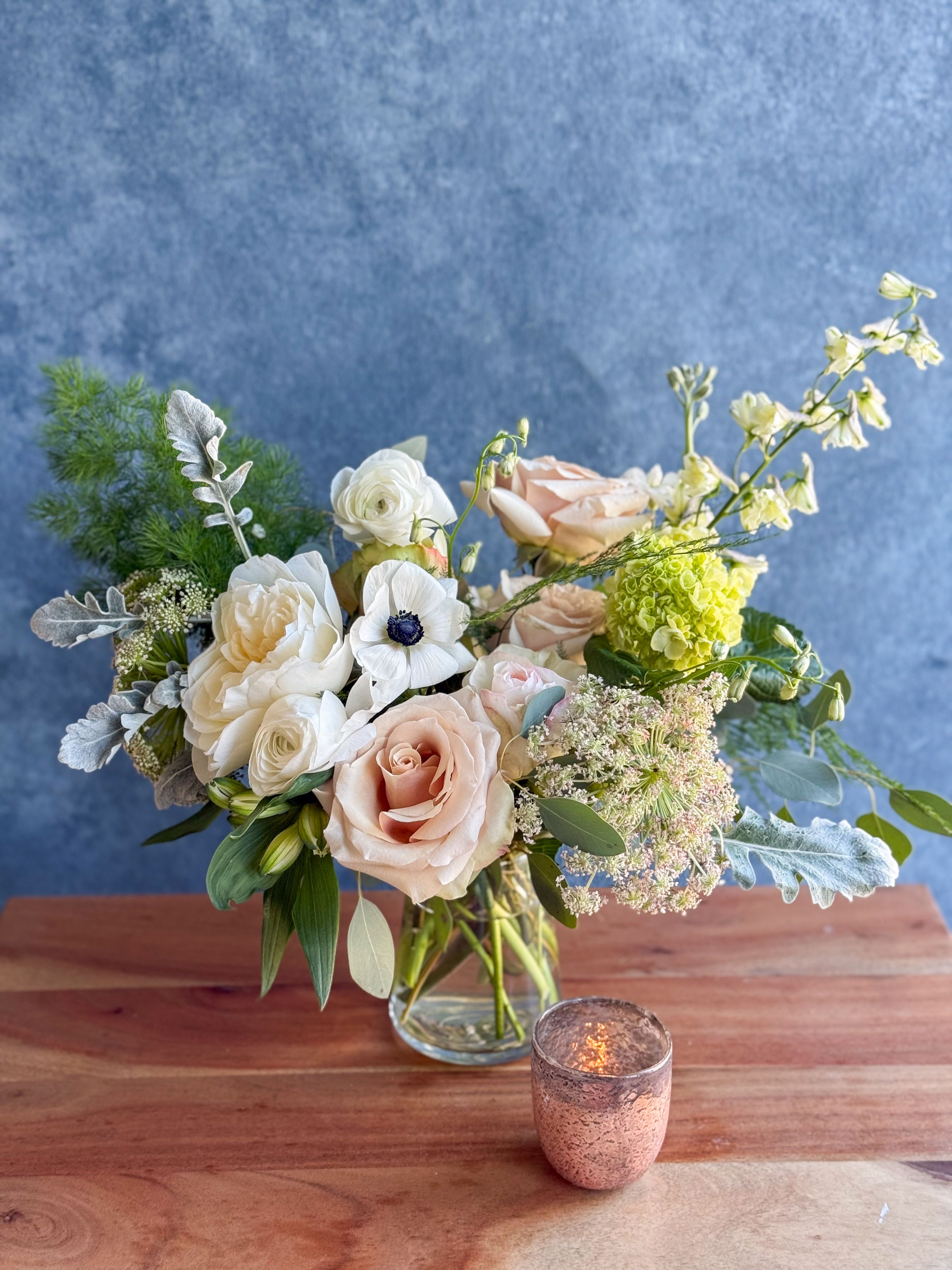 Blush and white bouquet in a clear glass vase with a small candle nearby