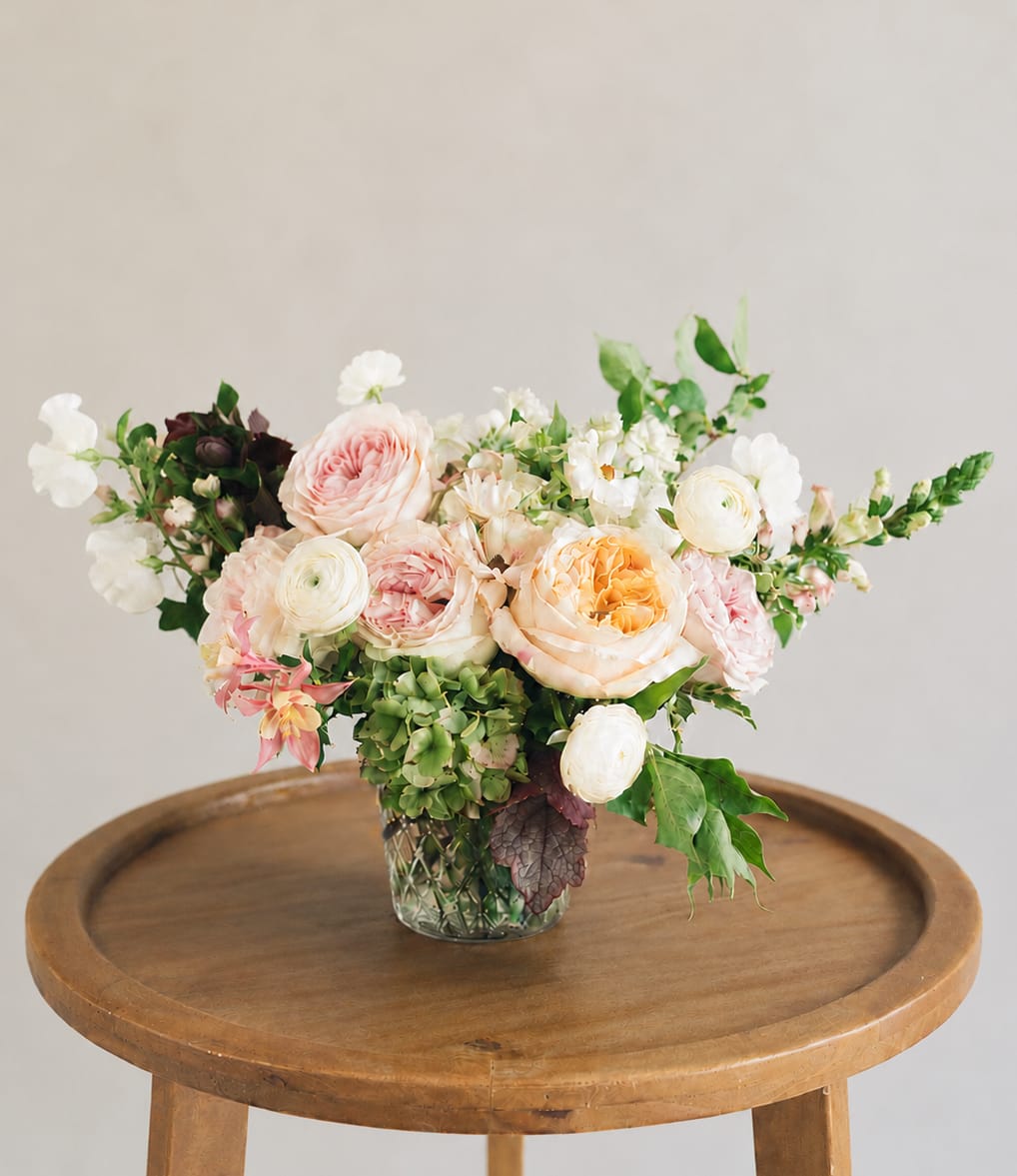 Mixed pastel flower arrangement in a glass vase on a wooden table