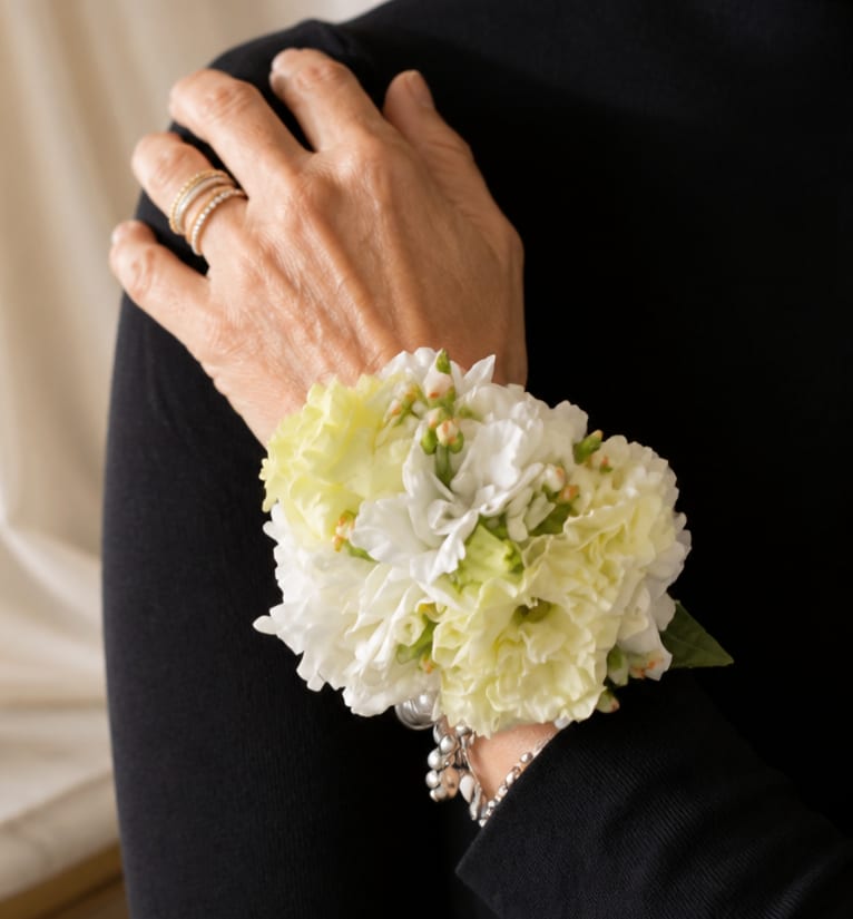 wrist corsage - lovely made to your request - Soft clusters of ruffled small flowers like spray roses, lisianthus form a compact wrist corsage that reads both elegant and effortless-perfect as a prom corsage, wedding accessory, or special-occasion wristpiece. Designed to sit neatly against the wrist on an elastic wristlet, this floral arrangement makes the person you're celebrating feel polished and cherished without overpowering their outfit.  The corsage features layered, ruffled blooms with small accent buds and touches of green foliage tucked through the cluster for a fresh, finished look. Its rounded, compact shape keeps the flowers close to the wrist for comfortable wear and a refined silhouette that complements formal attire. The elastic wristlet provides a secure, flexible fit for most wrists while keeping the arrangement positioned beautifully.  Choose this corsage to mark moments that deserve a delicate, traditional touch-mothers at graduations, bridesmaids at a wedding, or your student heading to prom. To ensure peak freshness, wear on the event day; if you need delivery or specific sizing notes for the wristlet, include them with your order and we'll accommodate your request.
