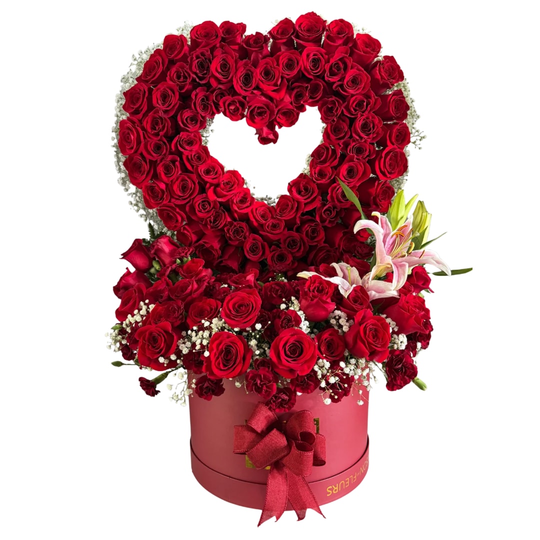 Heart-shaped red rose arrangement in a pink round box with lilies