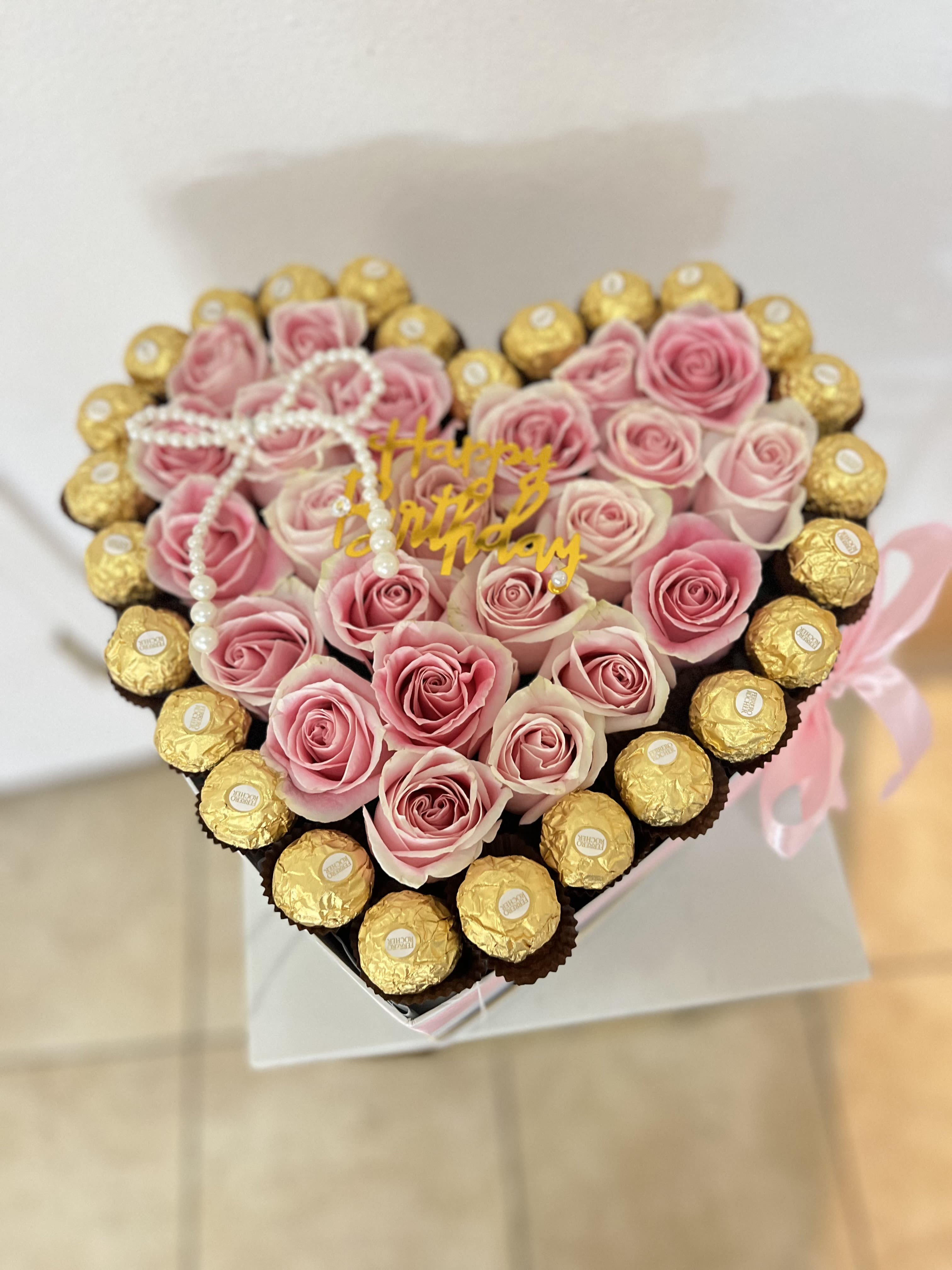 Heart-shaped arrangement of pink roses and gold-wrapped chocolates with a birthday topper