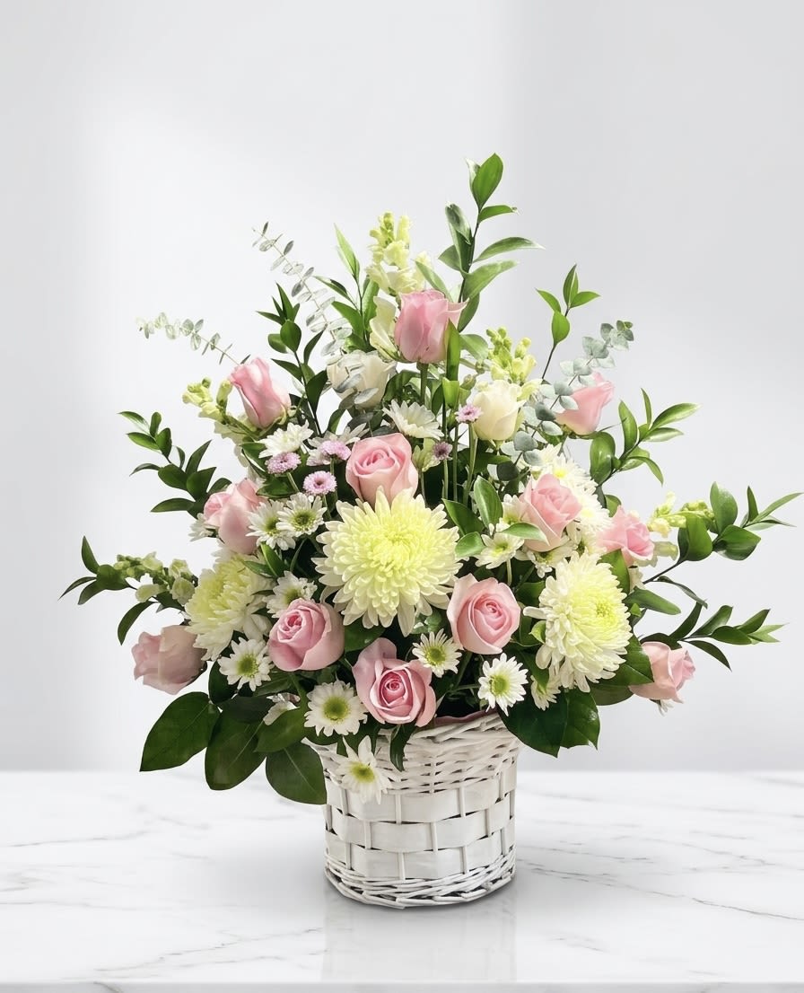 The Meadow Breeze Basket - This lush, garden-inspired vase arrangement is professionally designed in a classic white woven basket for a timeless look. As a premier local florist, we hand-select premium pink roses and large white spider mums to serve as the focal point, accented by delicate daisies, soaring snapdragons, and fragrant eucalyptus. Whether you are looking for a unique birthday gift or a custom floral centerpiece, this fresh flower arrangement is handcrafted to stand out. Our online flower shop specializes in ready-to-display designs that bring the beauty of a professional garden into any home. • Dimensions: Approximately 18" H x 14" W • Vessel: Reusable white wicker basket
