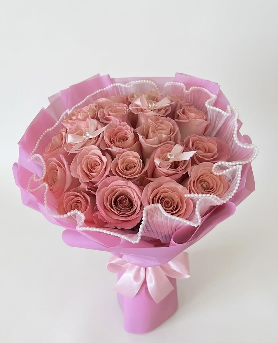 Pink Satin Serenade - A stunning Rose Bouquet  of dusty mauve roses, hand-tied and wrapped in vibrant pink luxury paper. This elegant bouquet features a unique pearl-edged tulle collar and delicate gemstone-centered bows, finished with a classic satin ribbon for a sophisticated, romantic aesthetic. (2 dozen count Roses)