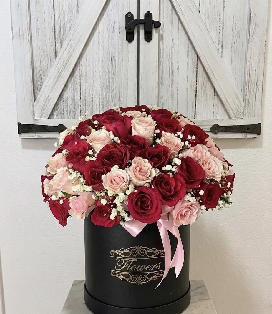 Romance in Bloom” Rose Hatbox Arrangement - Romance in Bloom” Rose Hatbox Arrangement  The “Romance in Bloom” arrangement is a luxurious blend of elegance and passion, perfect for celebrating love in its most beautiful form. Featuring a harmonious mix of deep red roses and soft blush pink roses, this bouquet is accented with red hypericum berries for texture and charm.