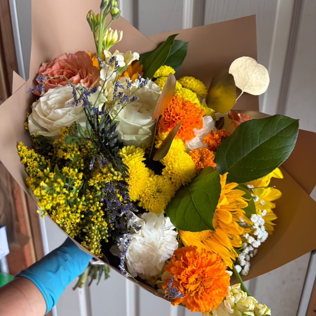 Mixed bouquet of roses, chrysanthemums, and carnations wrapped in brown paper