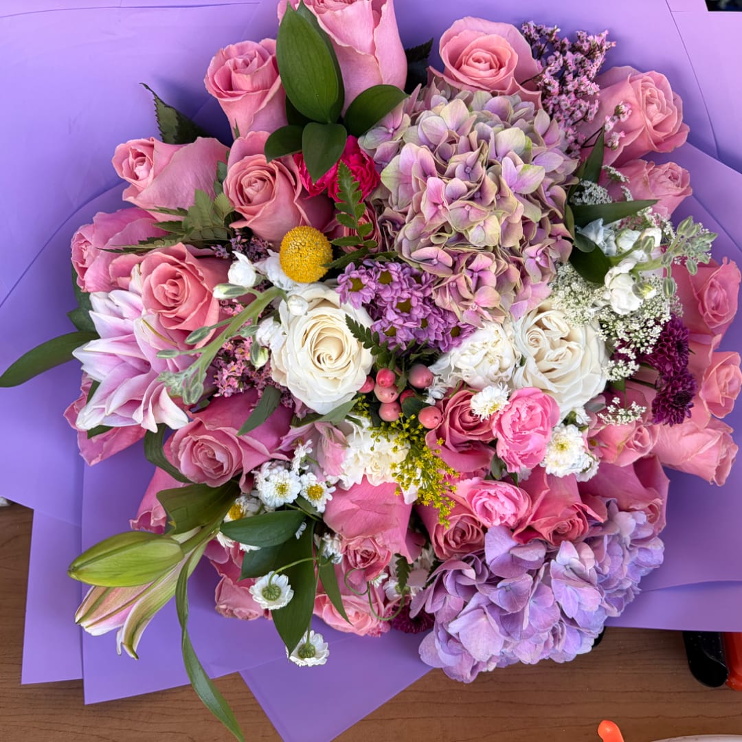 Pink and lavender bouquet with roses, hydrangeas, and lilies in purple wrap