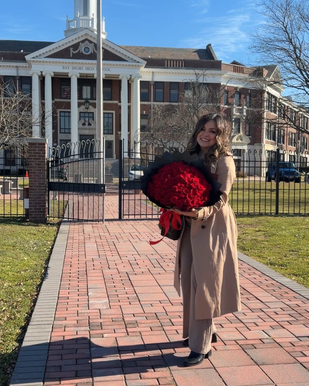 Woman holding a large bouquet of red roses in front of a school building