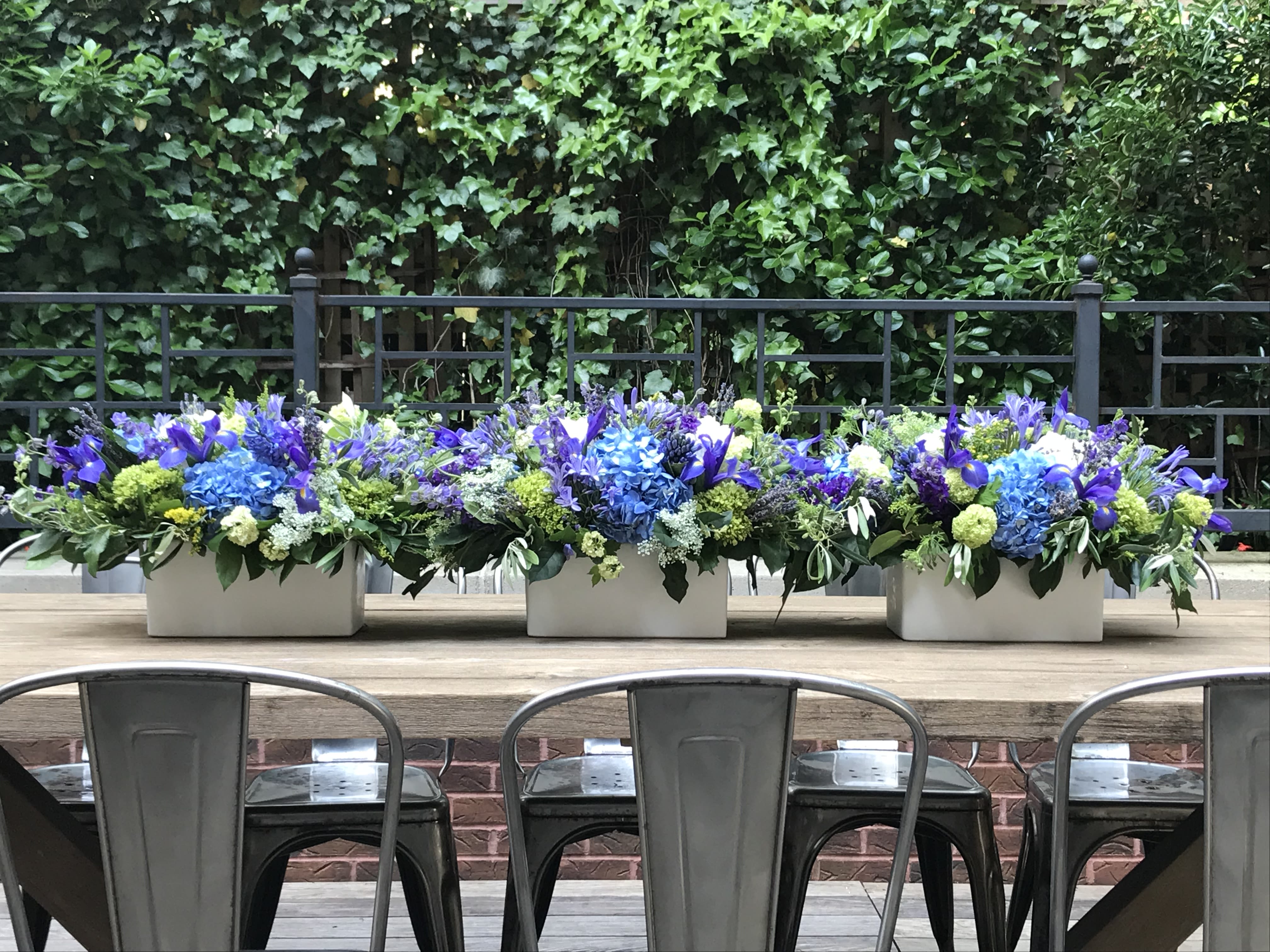 Three low floral centerpieces in white containers on a wooden table