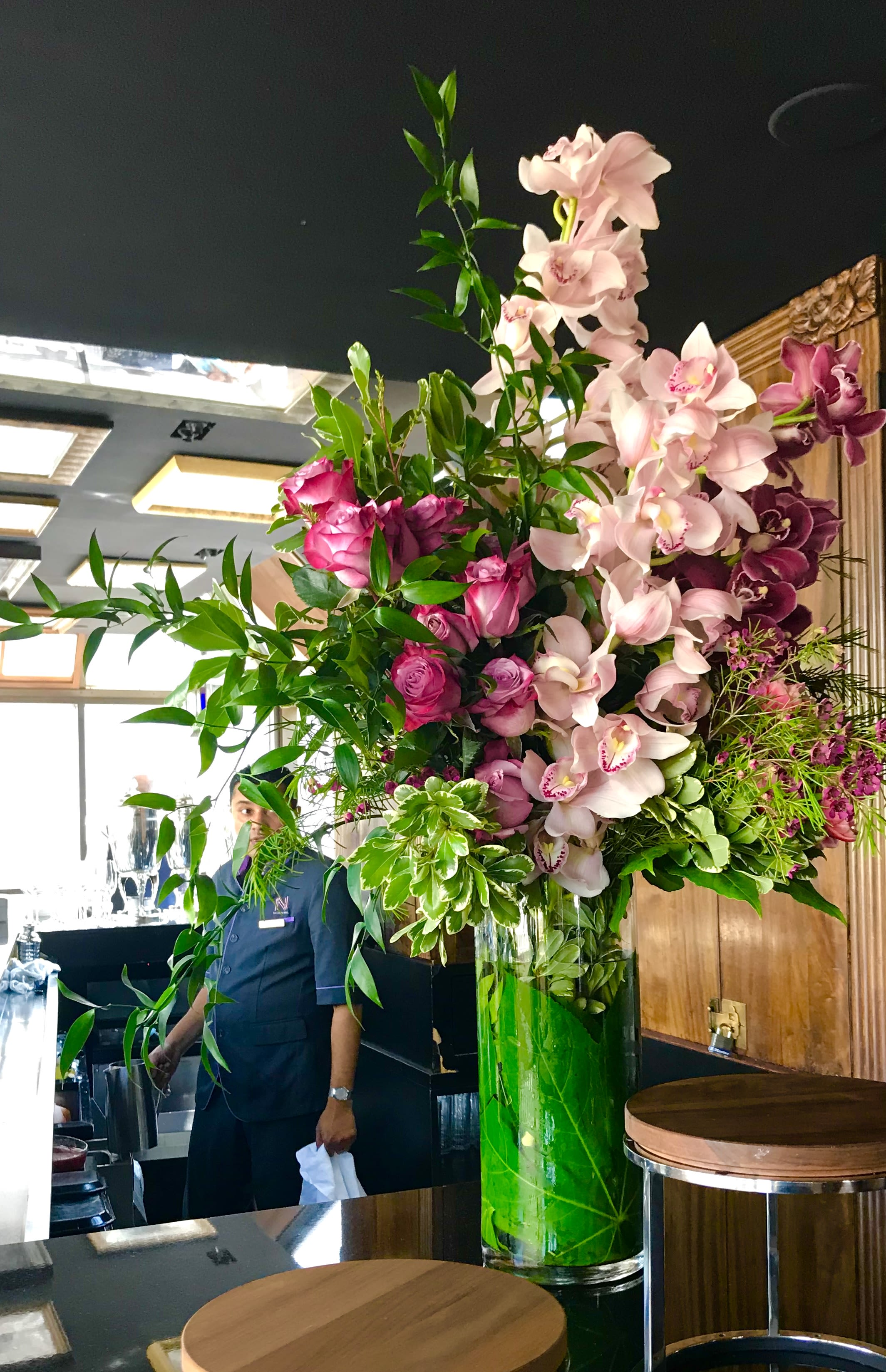 Tall floral arrangement with pink orchids and roses in a glass vase