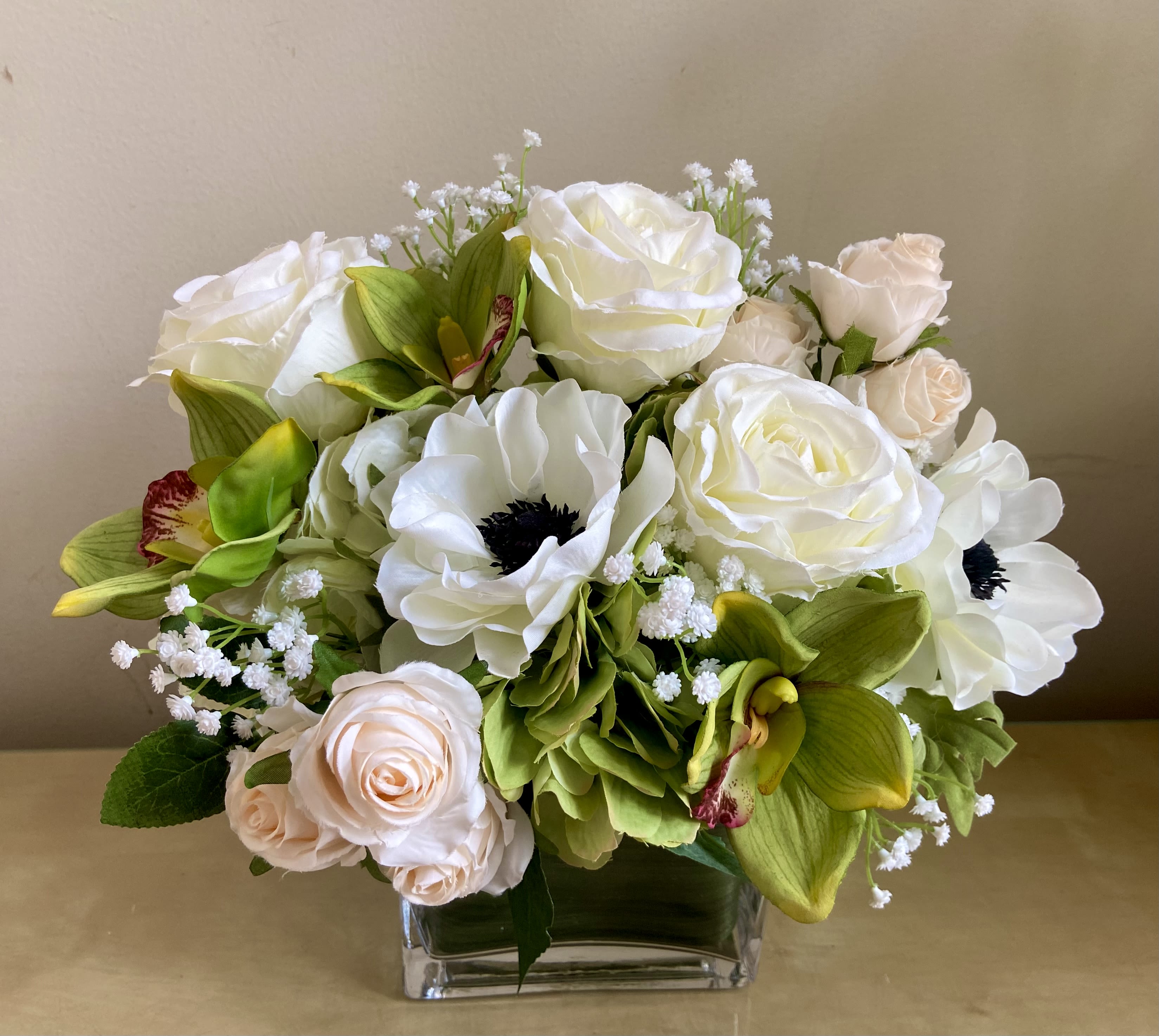 Low arrangement of white and blush roses with white anemones and green orchids in a clear glass vase.