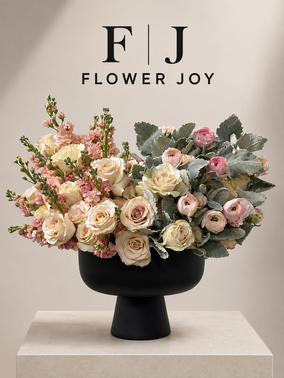 Cream and pink roses with ranunculus in a black pedestal vase
