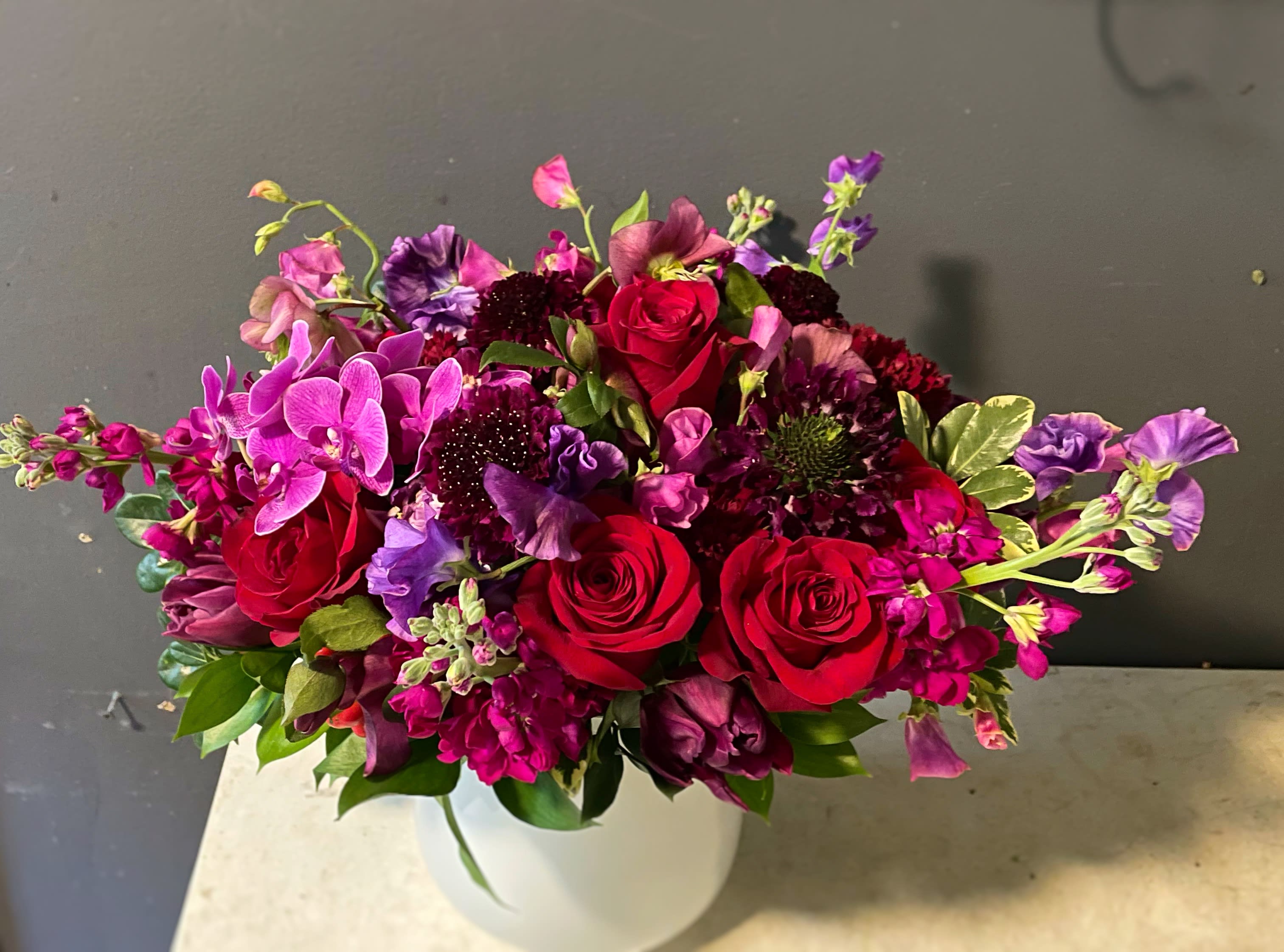 Bouquet of red roses and purple flowers in a white vase