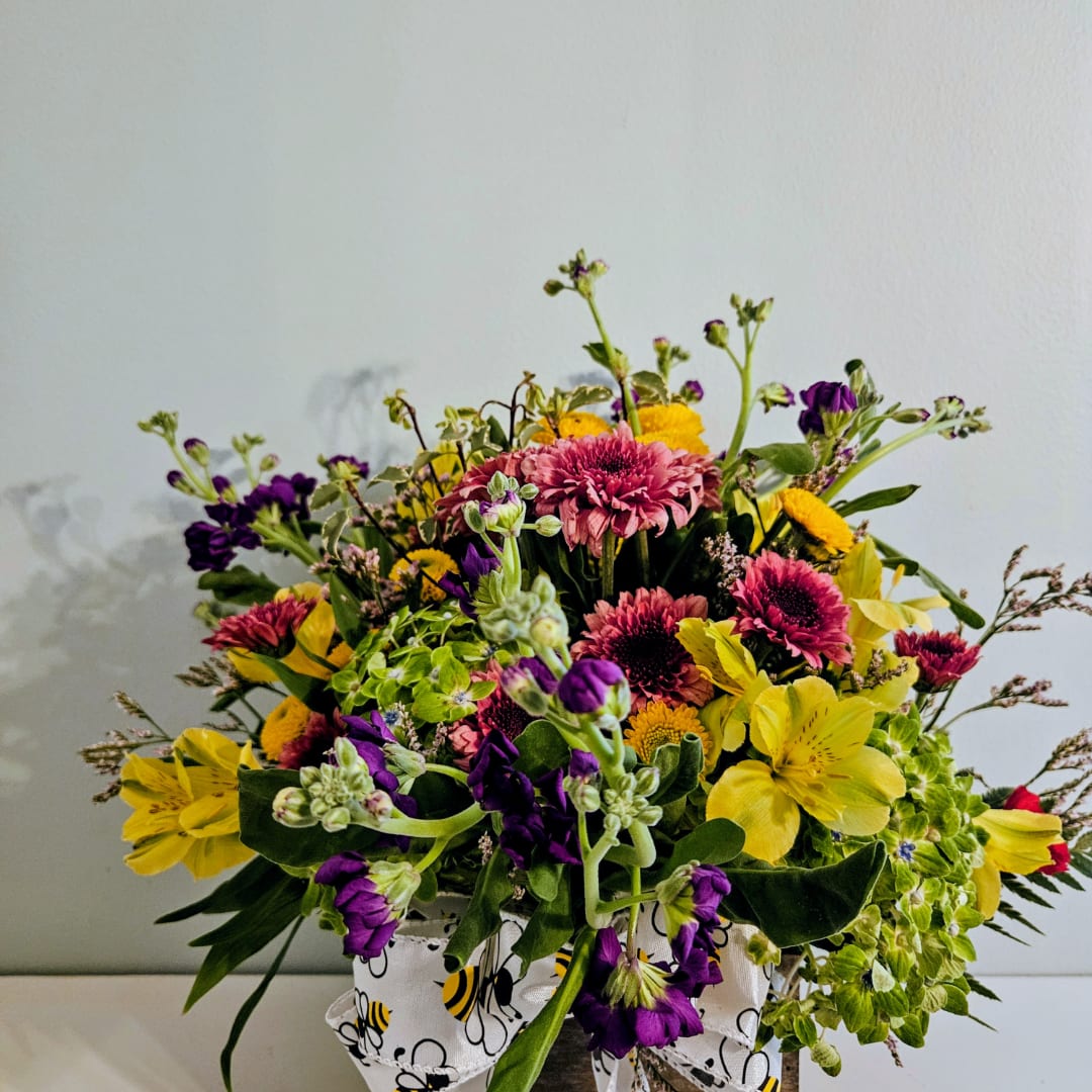 Mixed bouquet of yellow, pink, and purple flowers in a bee-patterned container
