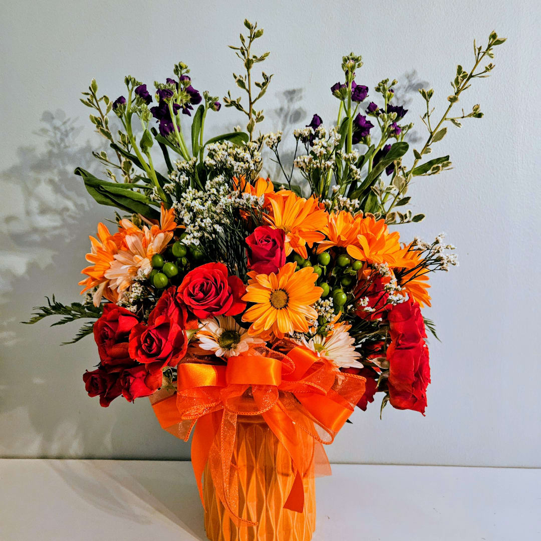 Bouquet of red roses and orange daisies in a glass vase with an orange ribbon