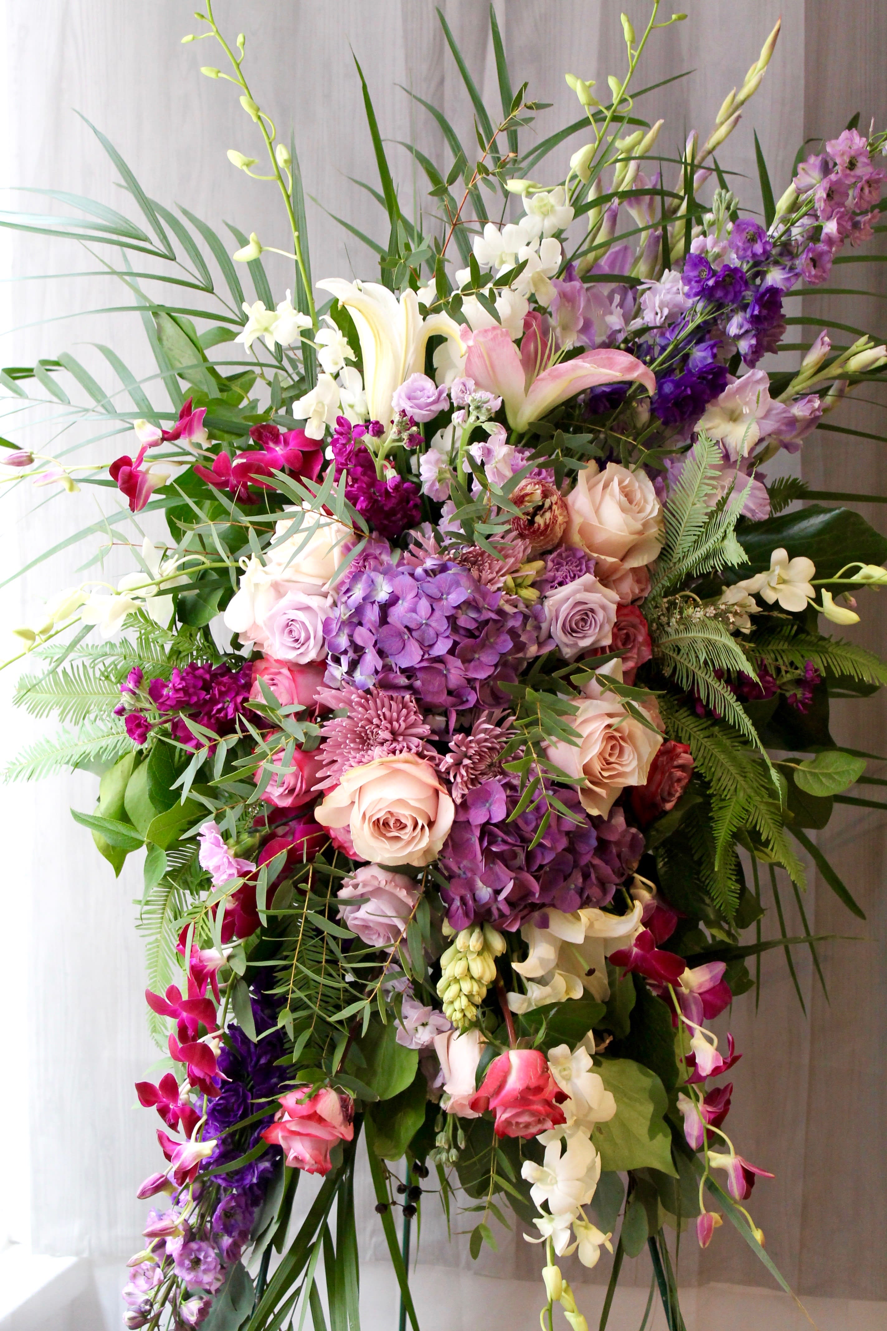 Large mixed floral arrangement with roses, lilies, orchids, and purple hydrangea