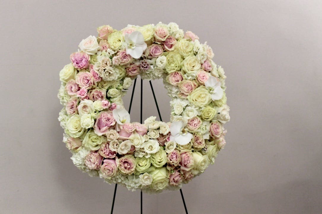 Circular floral wreath of pink and cream roses on a black stand