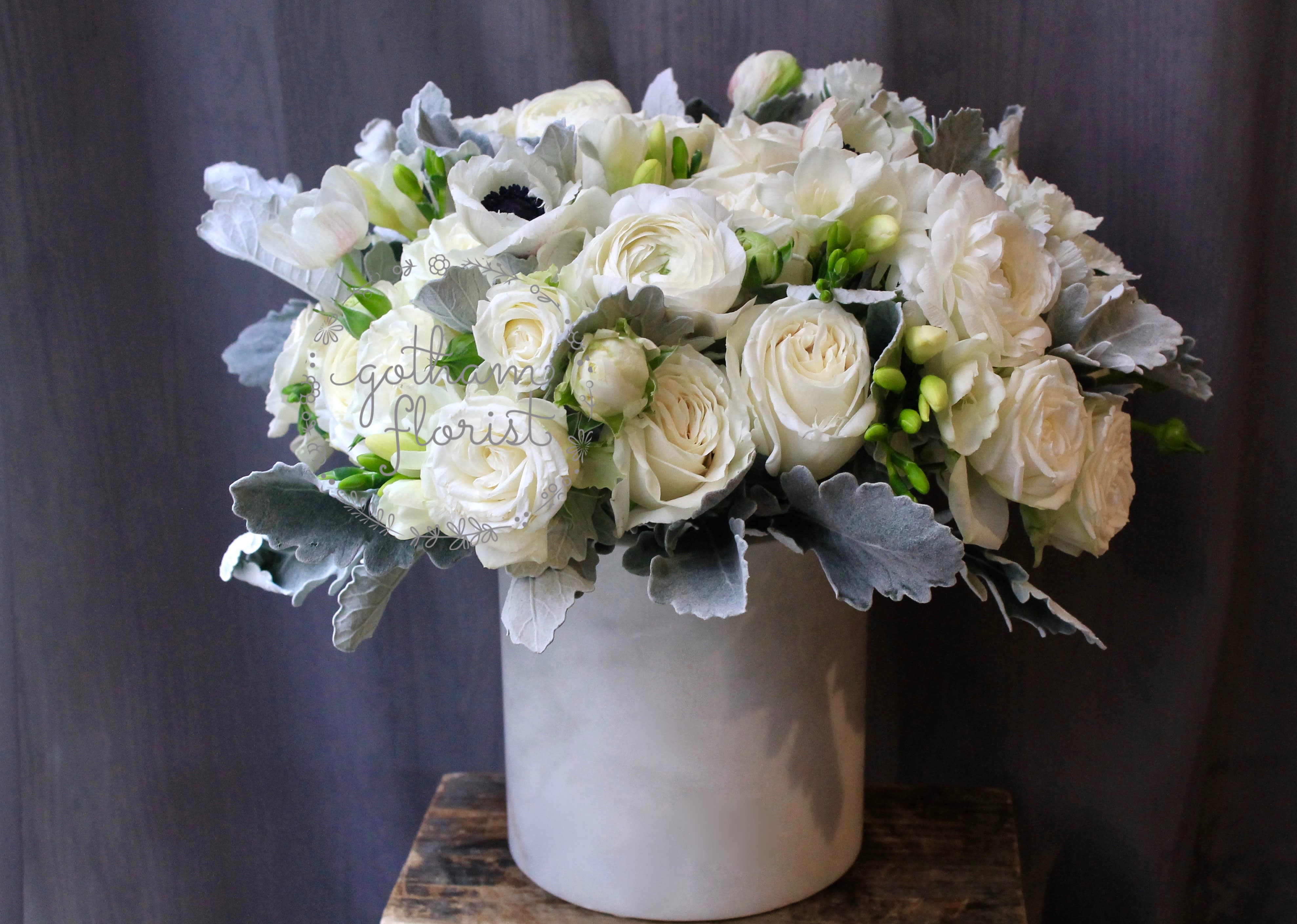 White rose bouquet in a tall gray vase with silver foliage