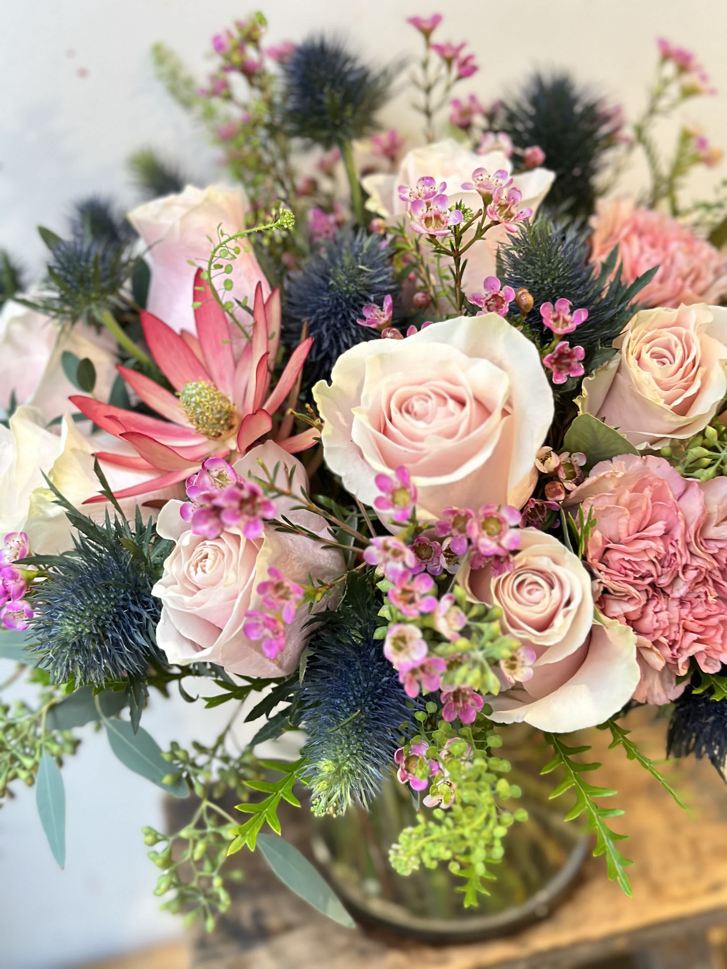 Bouquet of pale pink roses and pink blooms with blue thistle in a vase