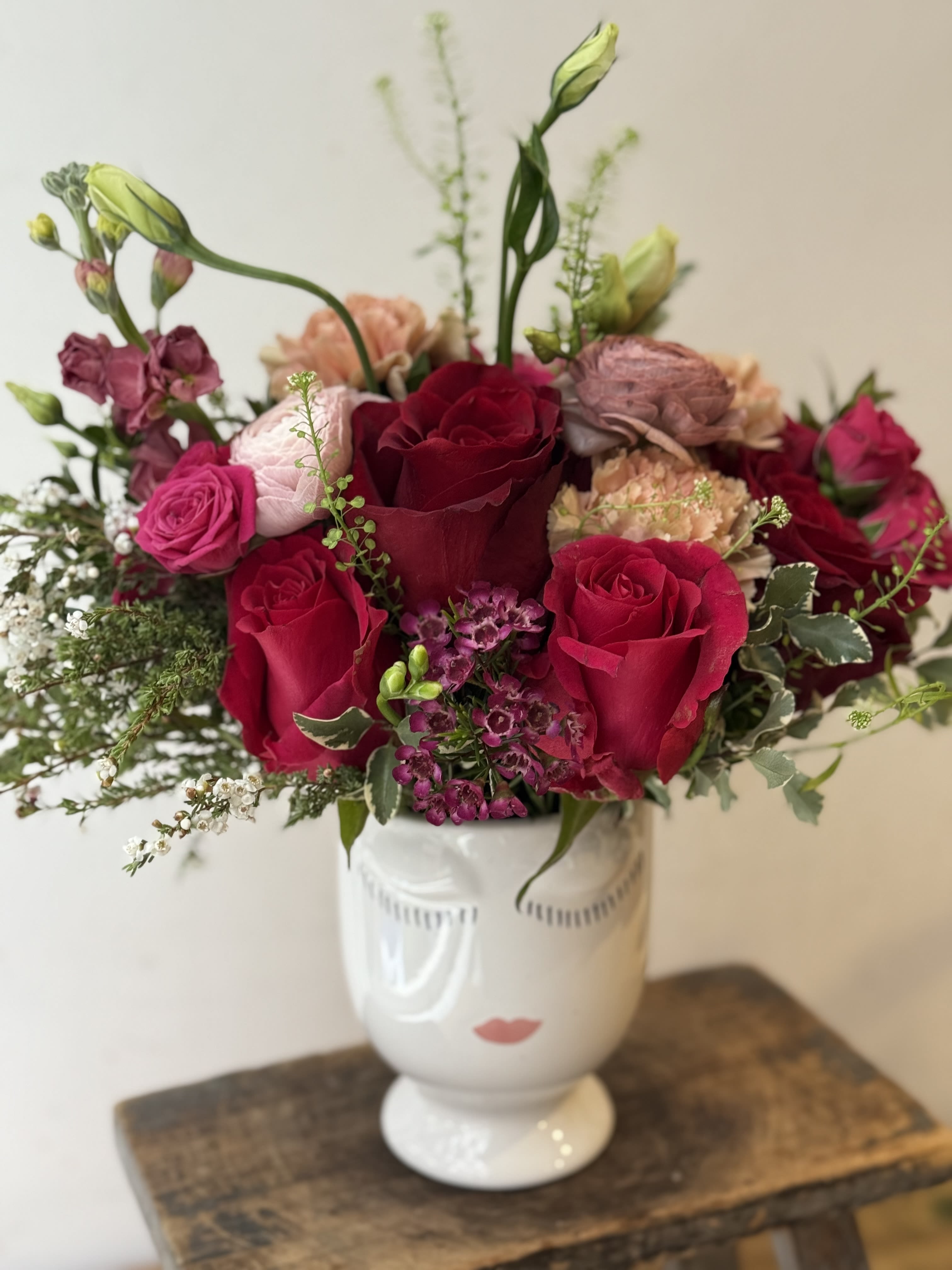 Bouquet of red and pink roses in a white vase with a face design