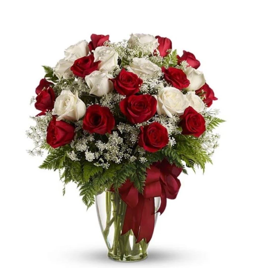 Red and white roses arranged in a clear glass vase with a red ribbon