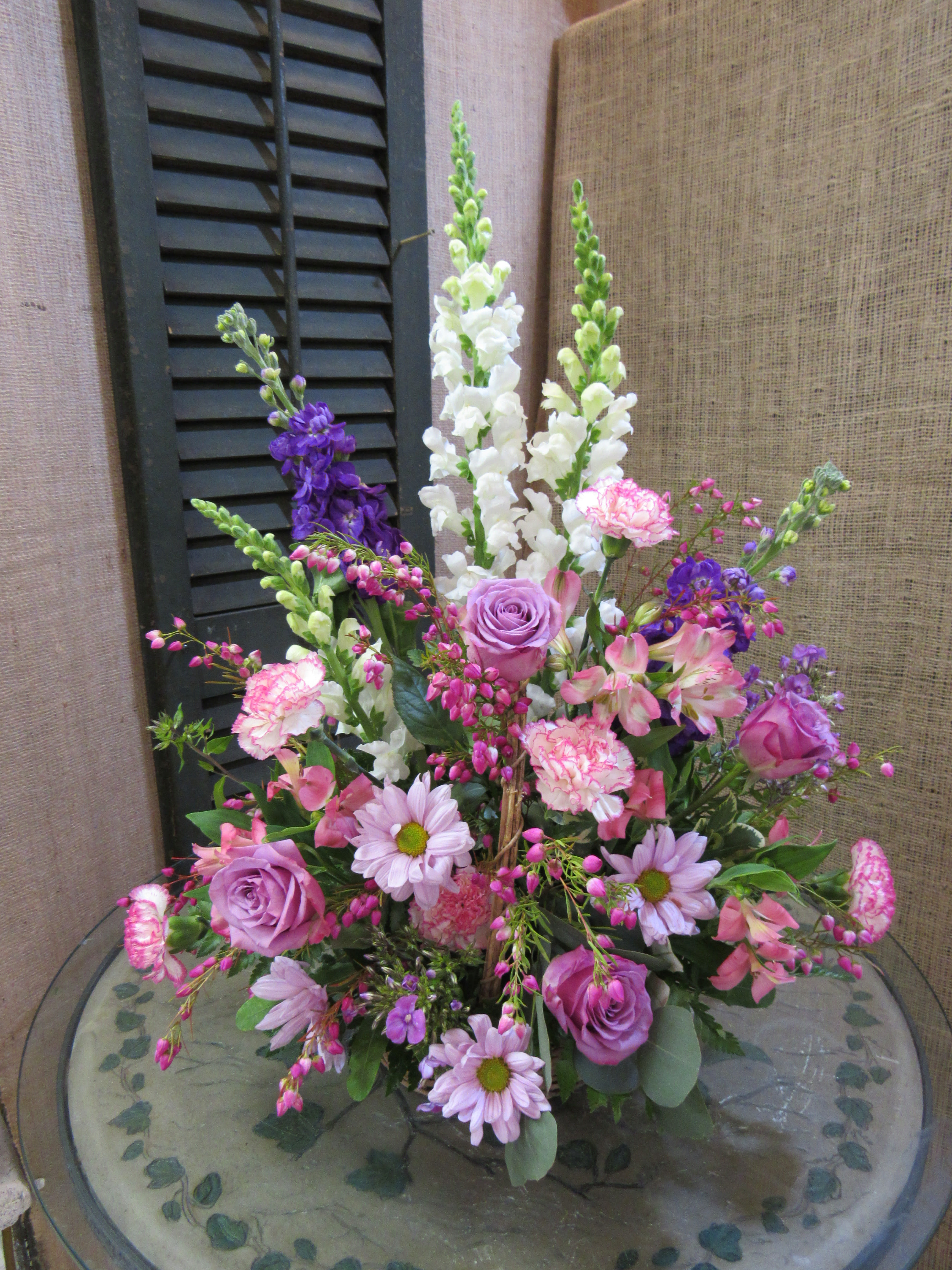 Mixed pink and purple floral arrangement with tall white spikes in a glass vase