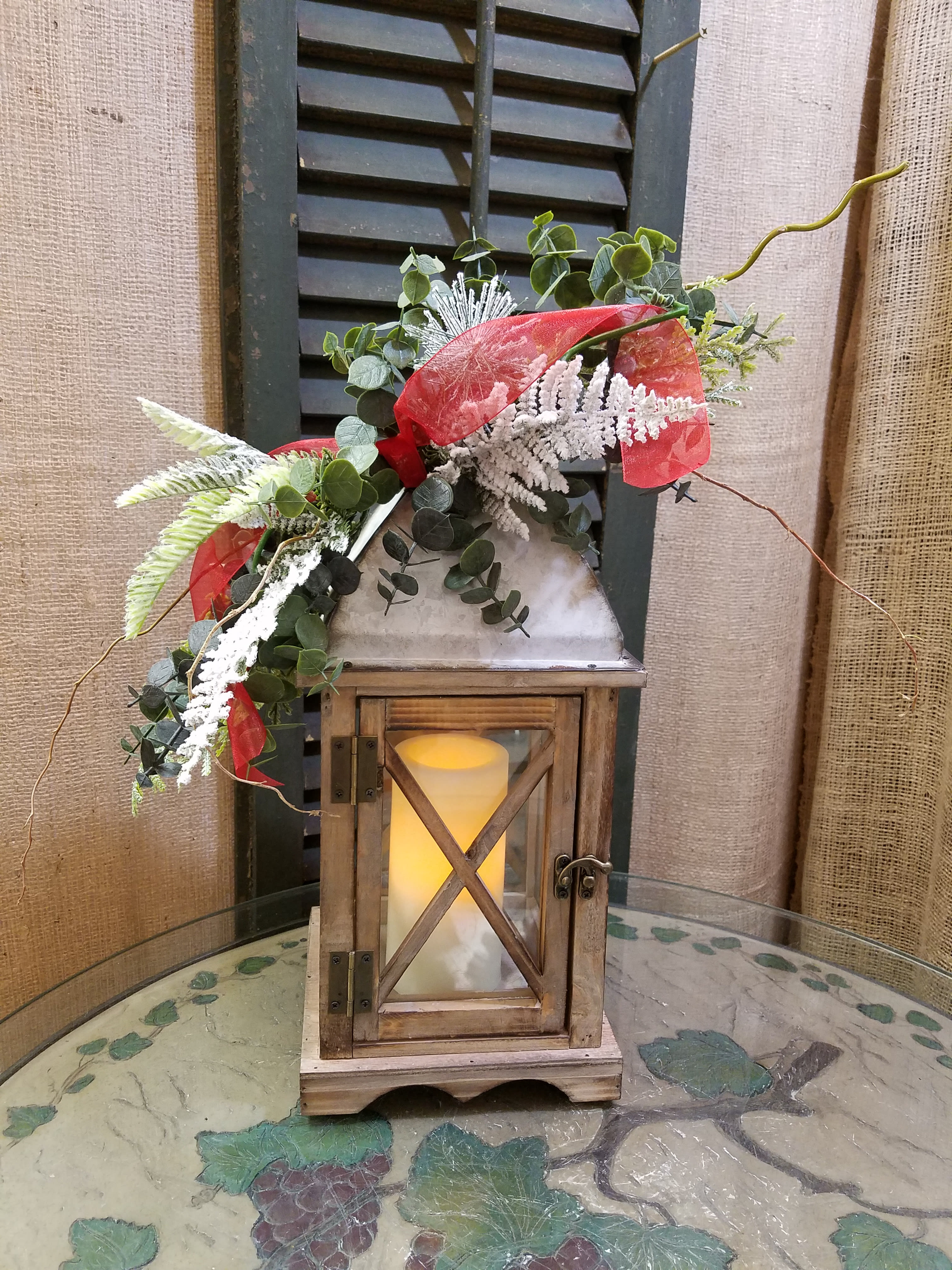 Lantern with greenery and red ribbon on a table