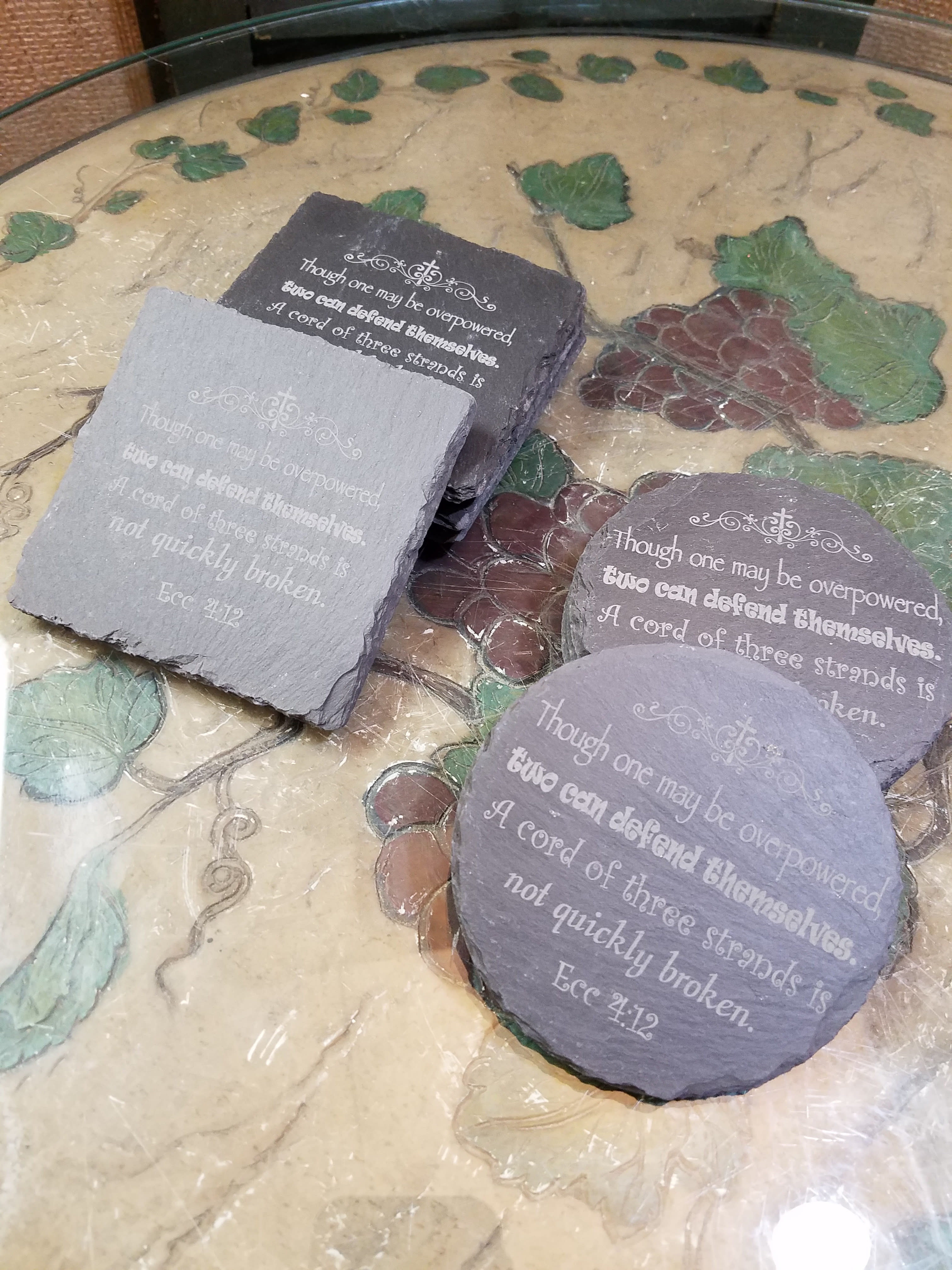 Four engraved slate coasters with a Bible verse on a decorative table.