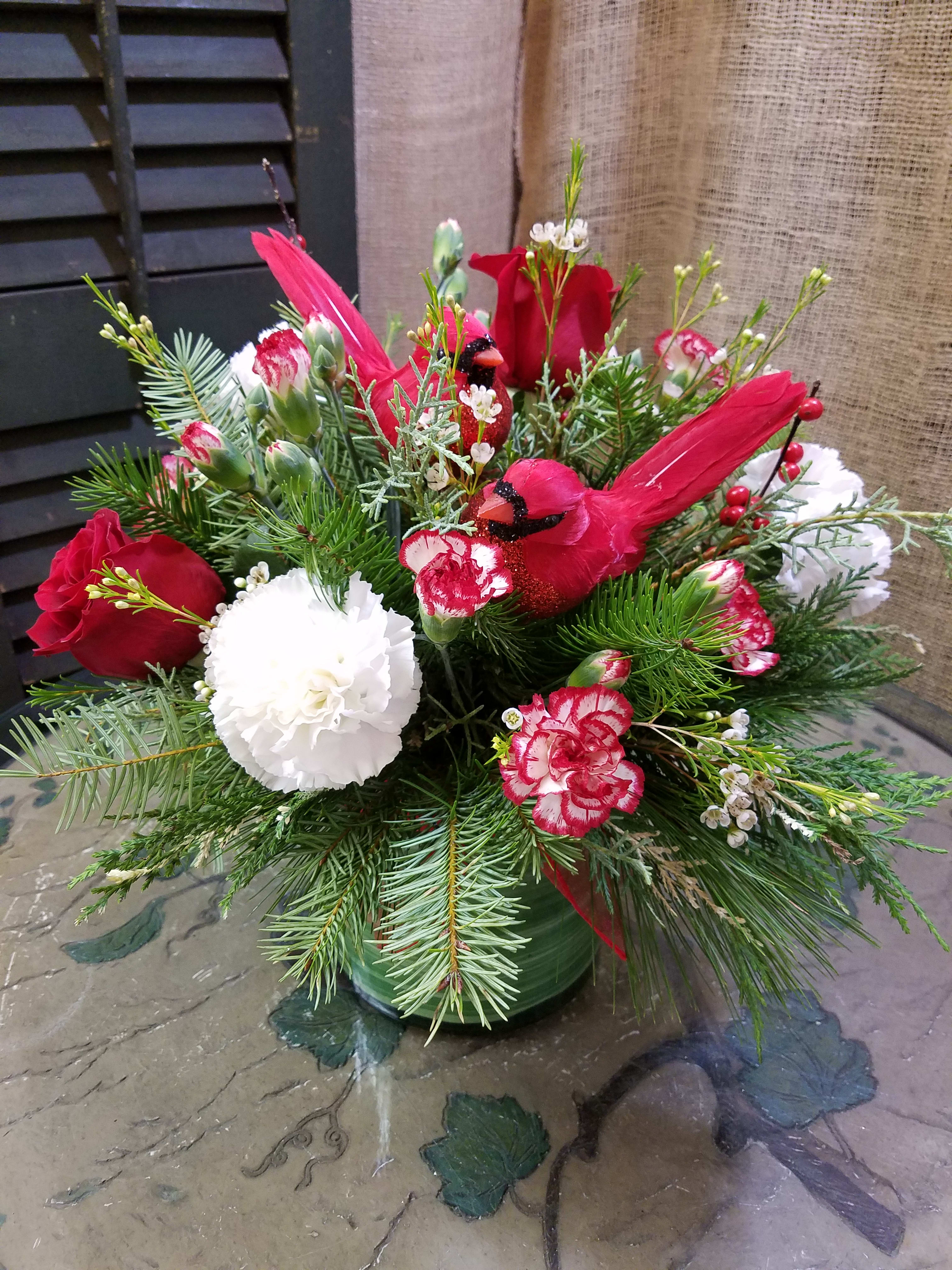 Holiday arrangement with red cardinals, roses, and white carnations in a green vase