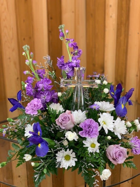 Purple and white floral arrangement with a clear glass cross centerpiece