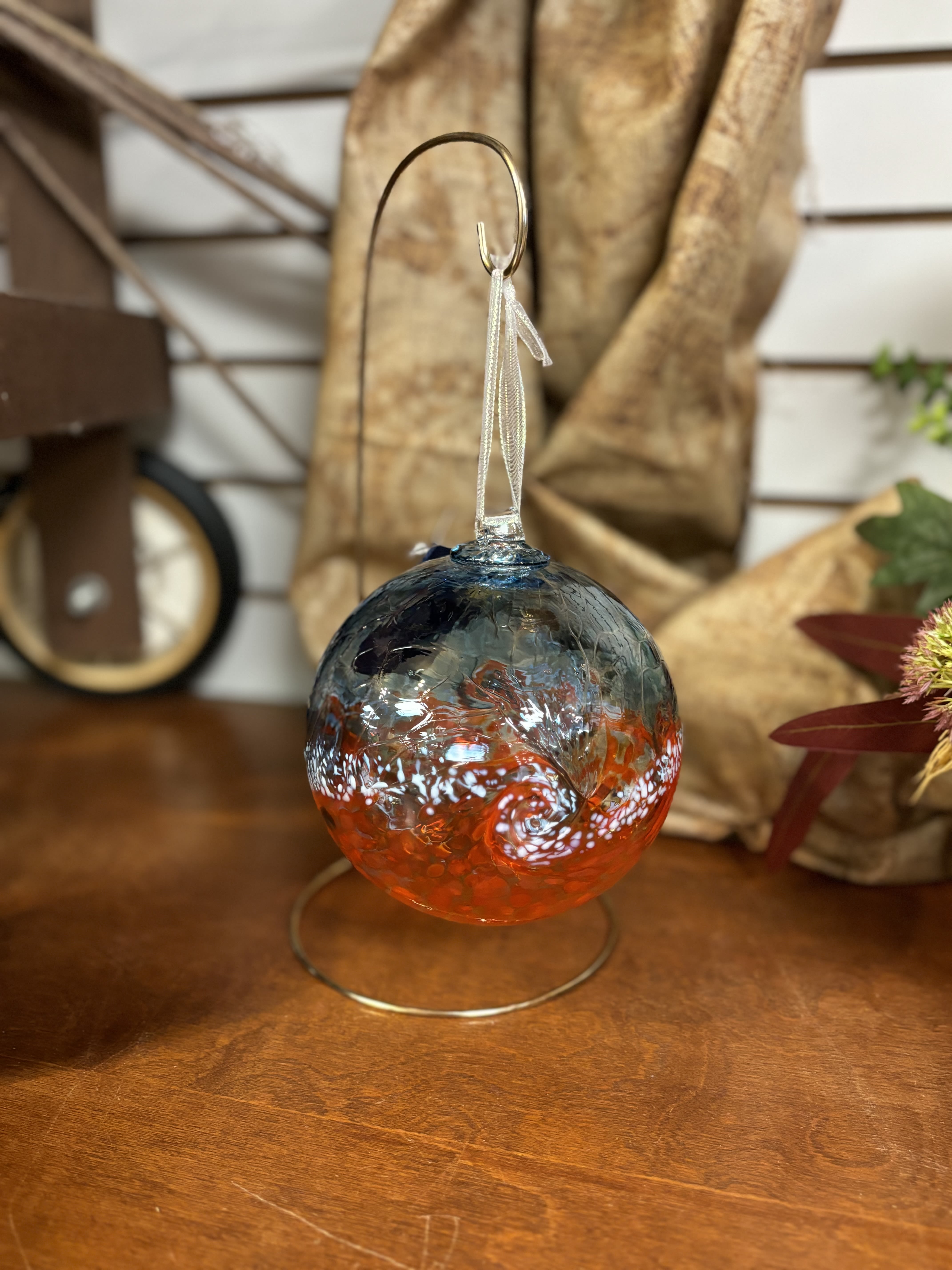 Glass ornament with blue and orange swirls hanging on a metal stand