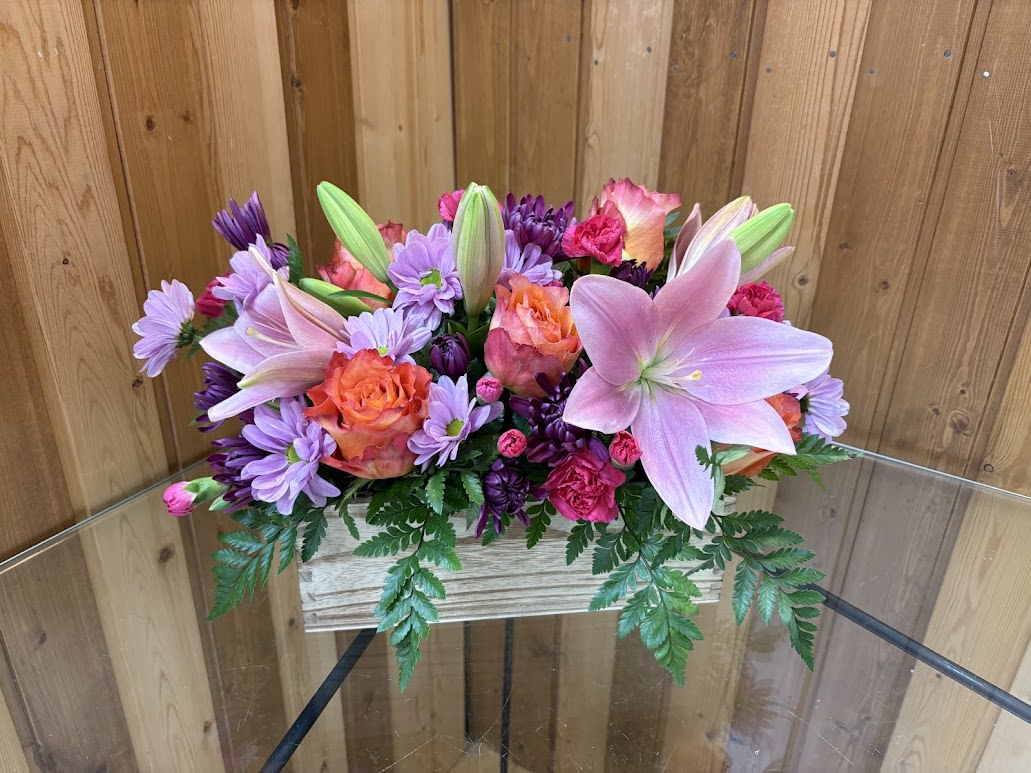 Low arrangement of pink lilies, orange roses, and purple mums in a rustic wooden box