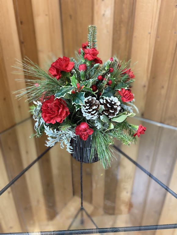 Holiday arrangement with red carnations, pinecones, and evergreen in a black container
